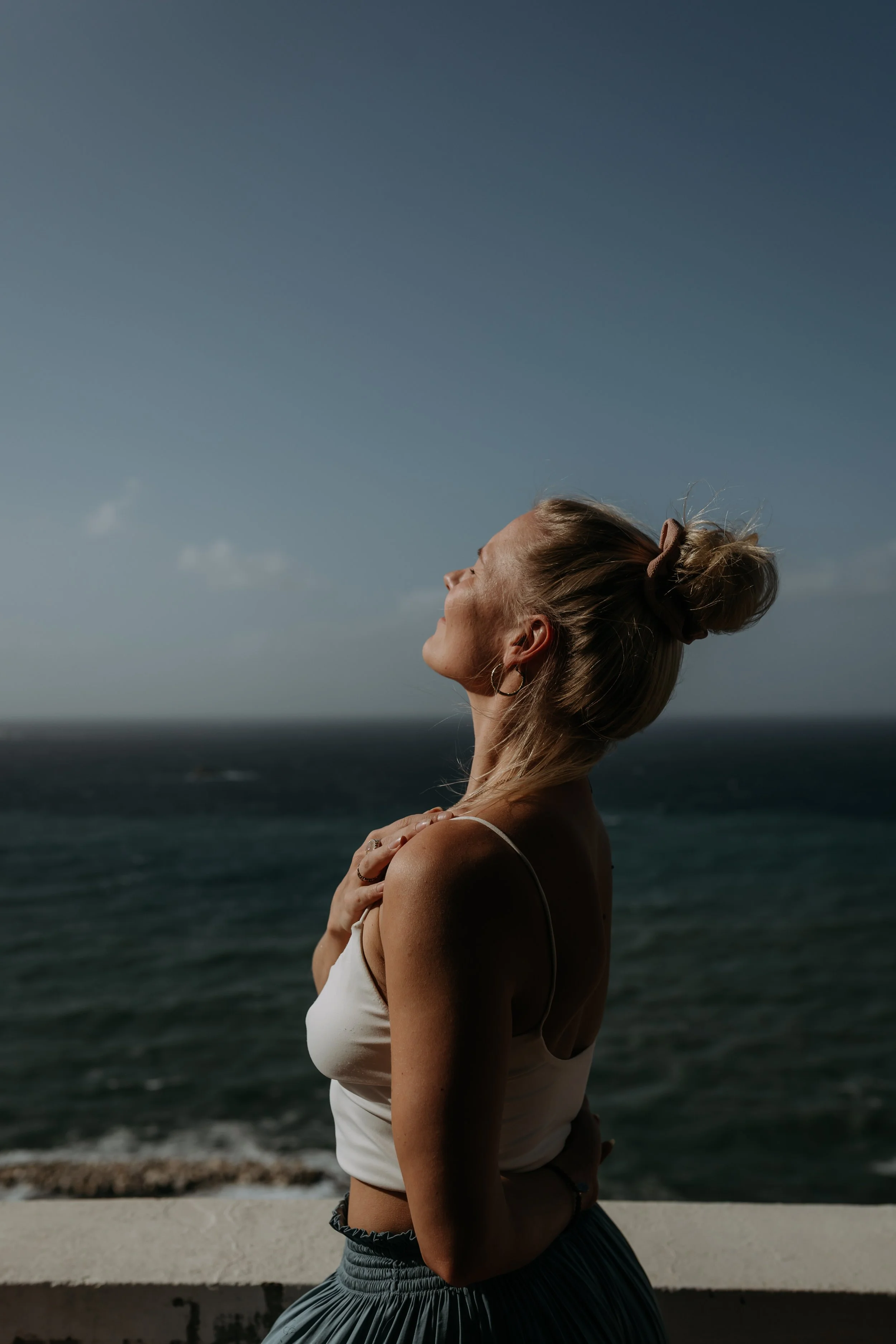 Vaimo katsoo iloisesti taivasta ja nauttii merinäköalasta.