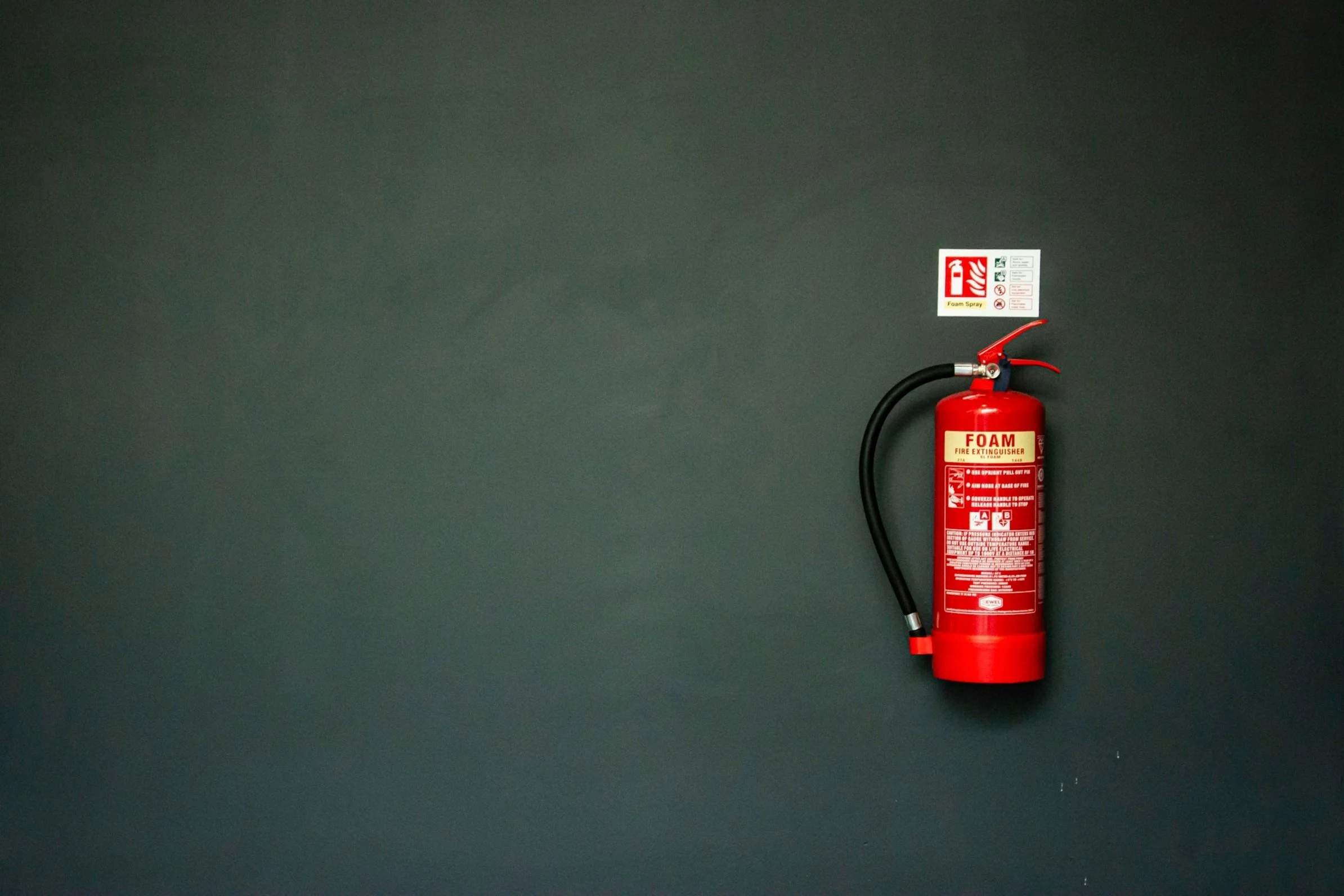 Red foam fire extinguisher mounted on a dark green wall, with an instruction label above it.