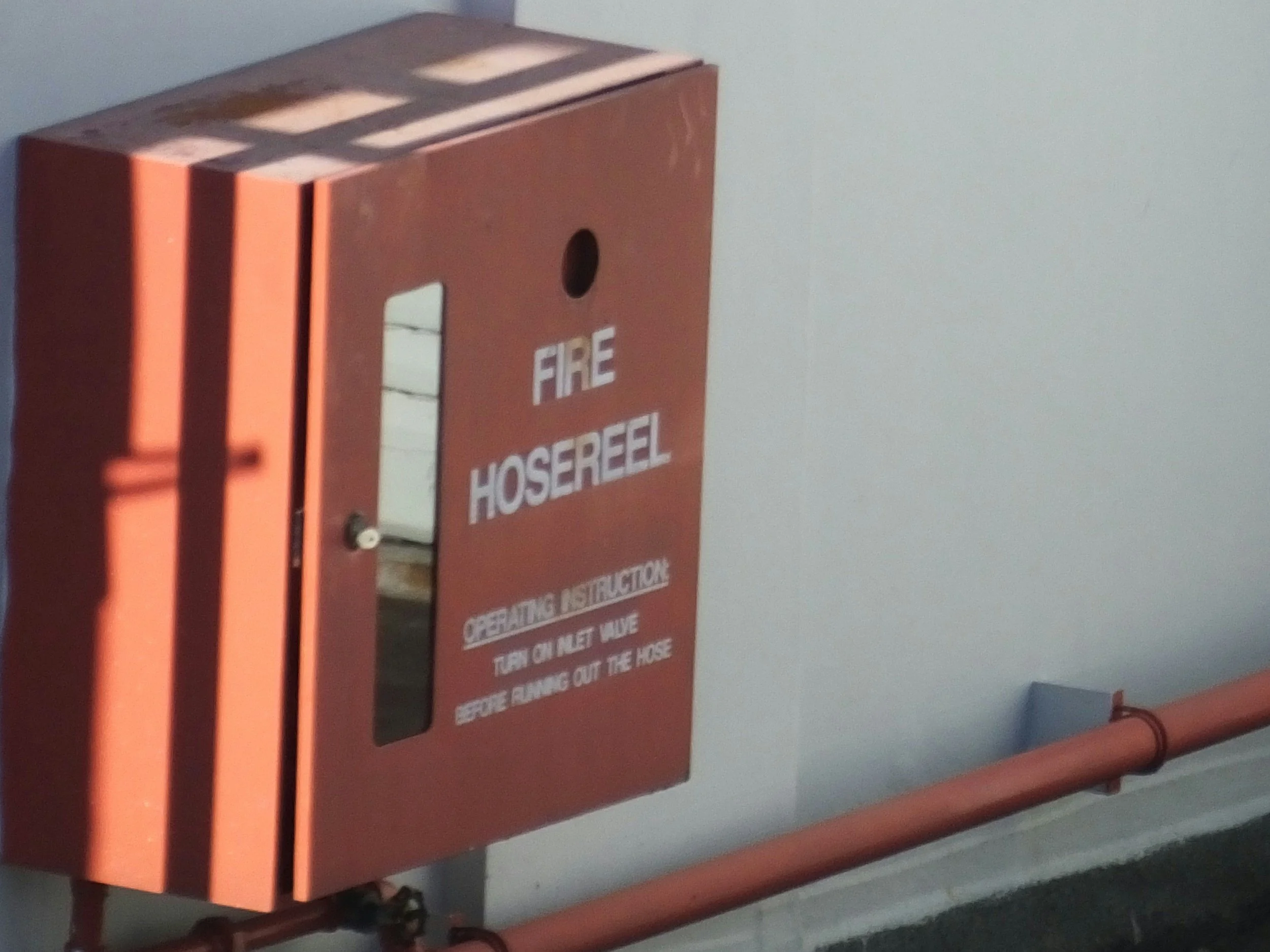 Red fire hose reel cabinet mounted on a wall with a pipe below it.