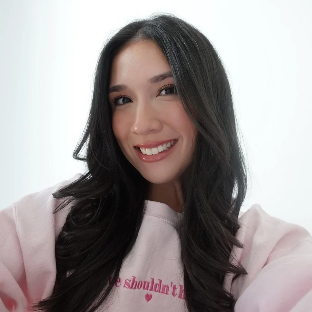A woman with long dark hair smiling at the camera, wearing a light pink shirt.