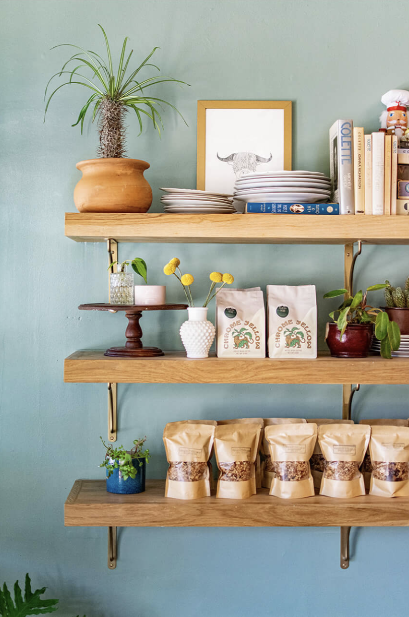 Interior shelves at Colette Bread & Bakeshop displaying granola bags, Chrome Yellow coffee, ceramics, and plants
