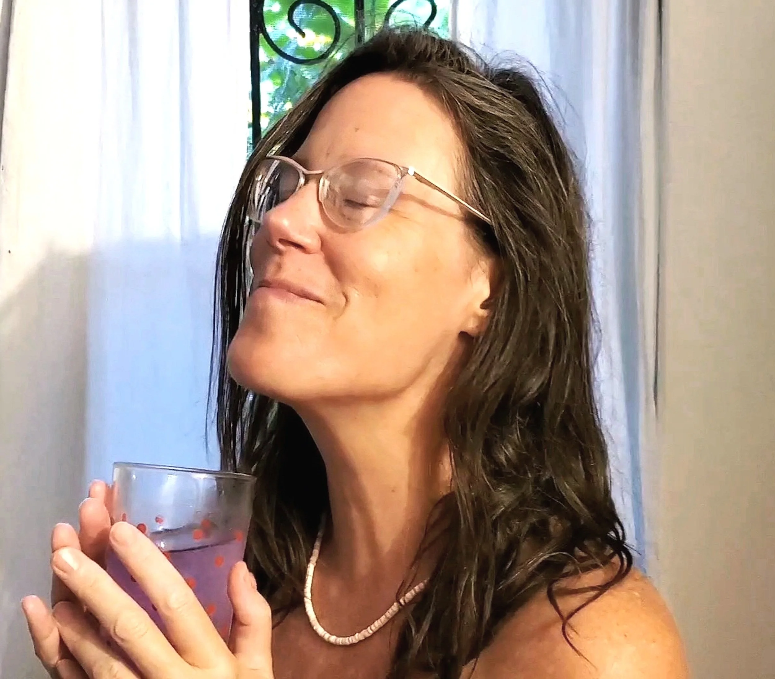 headshot of light-skinned femme with glasses and brown hair, eyes closed tasting of Transformation Tea