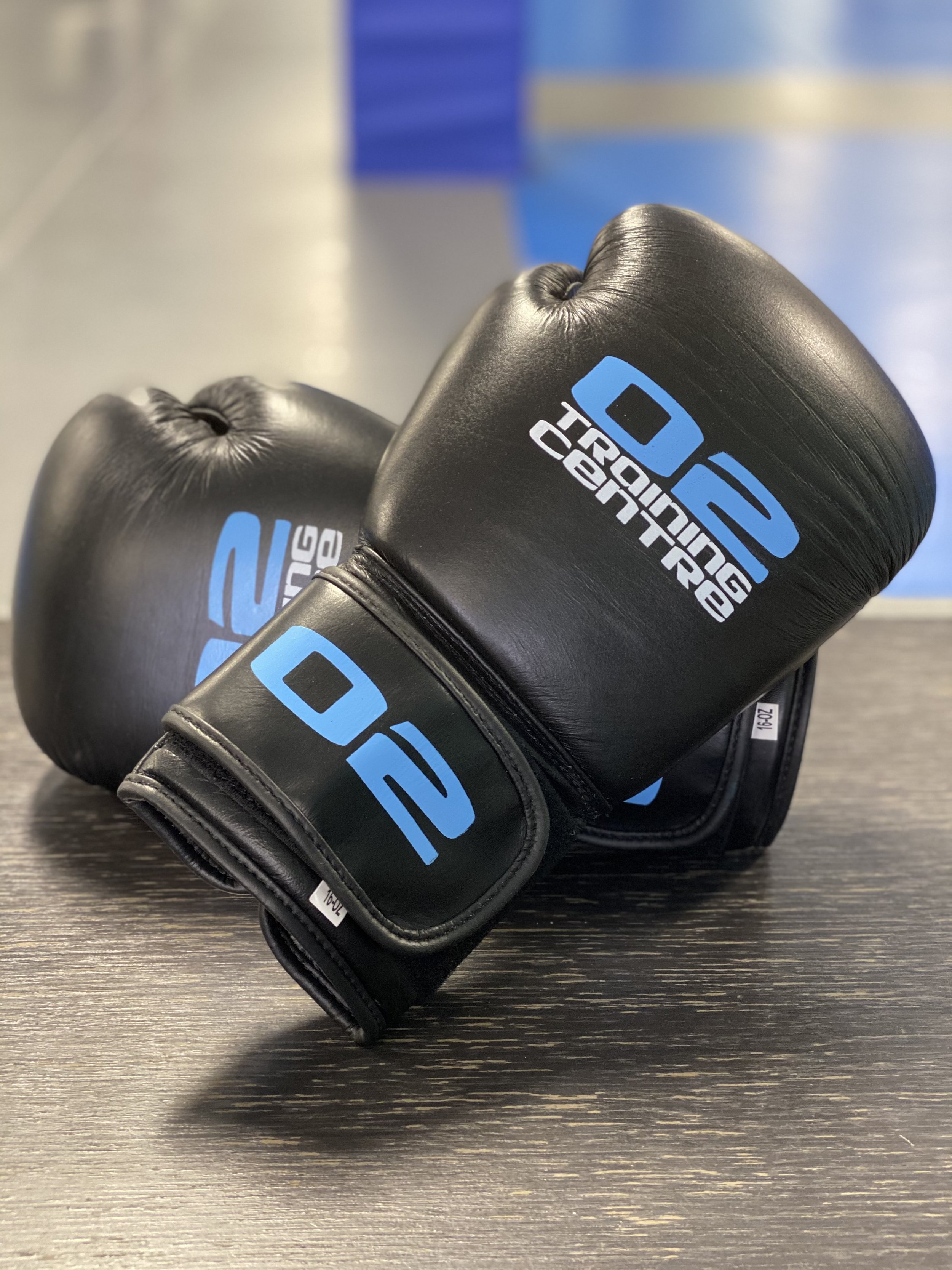 Black boxing gloves with blue and white logo resting on a dark wooden surface.
