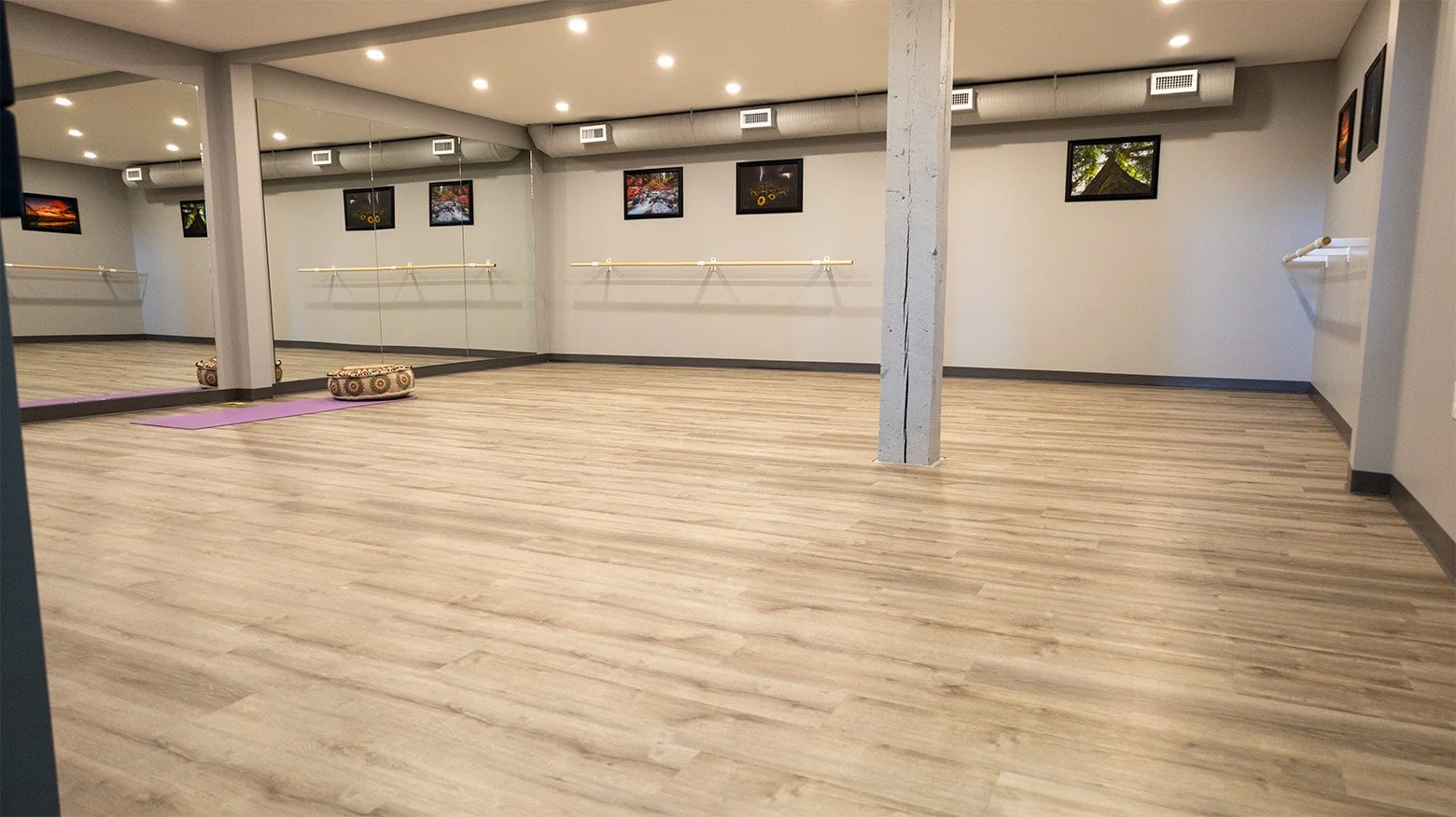 Empty dance studio with large mirrors, wooden flooring, ballet barres, and picture frames on the wall.