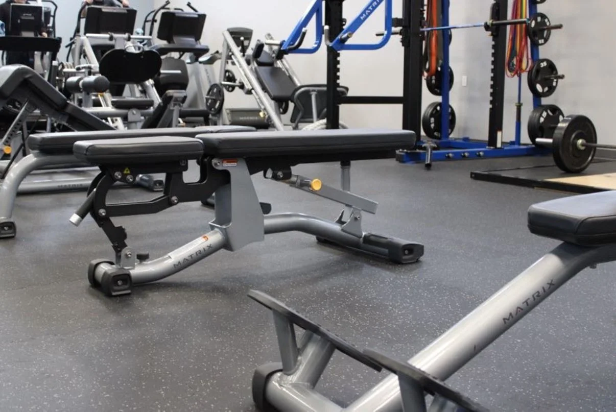 Empty gym with workout benches, weightlifting equipment, and weight plates in the background.