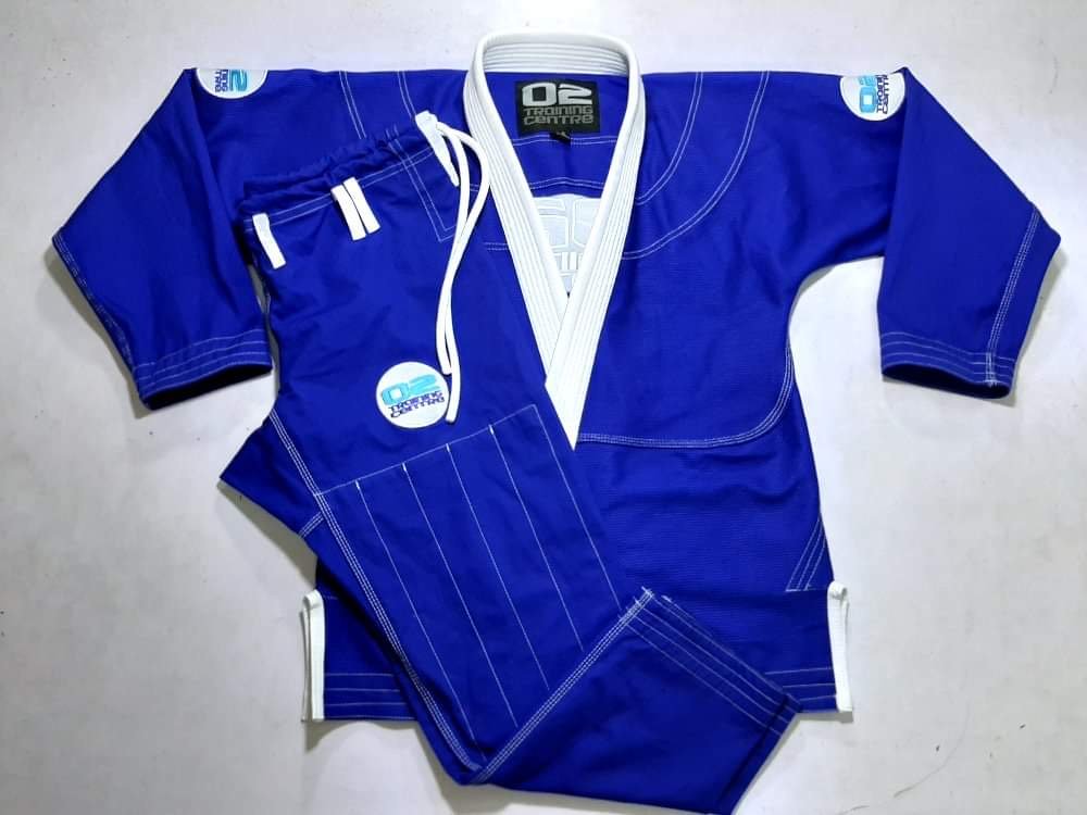 A blue Brazilian jiu-jitsu gi with white accents, featuring training center logos on the shoulders and chest.
