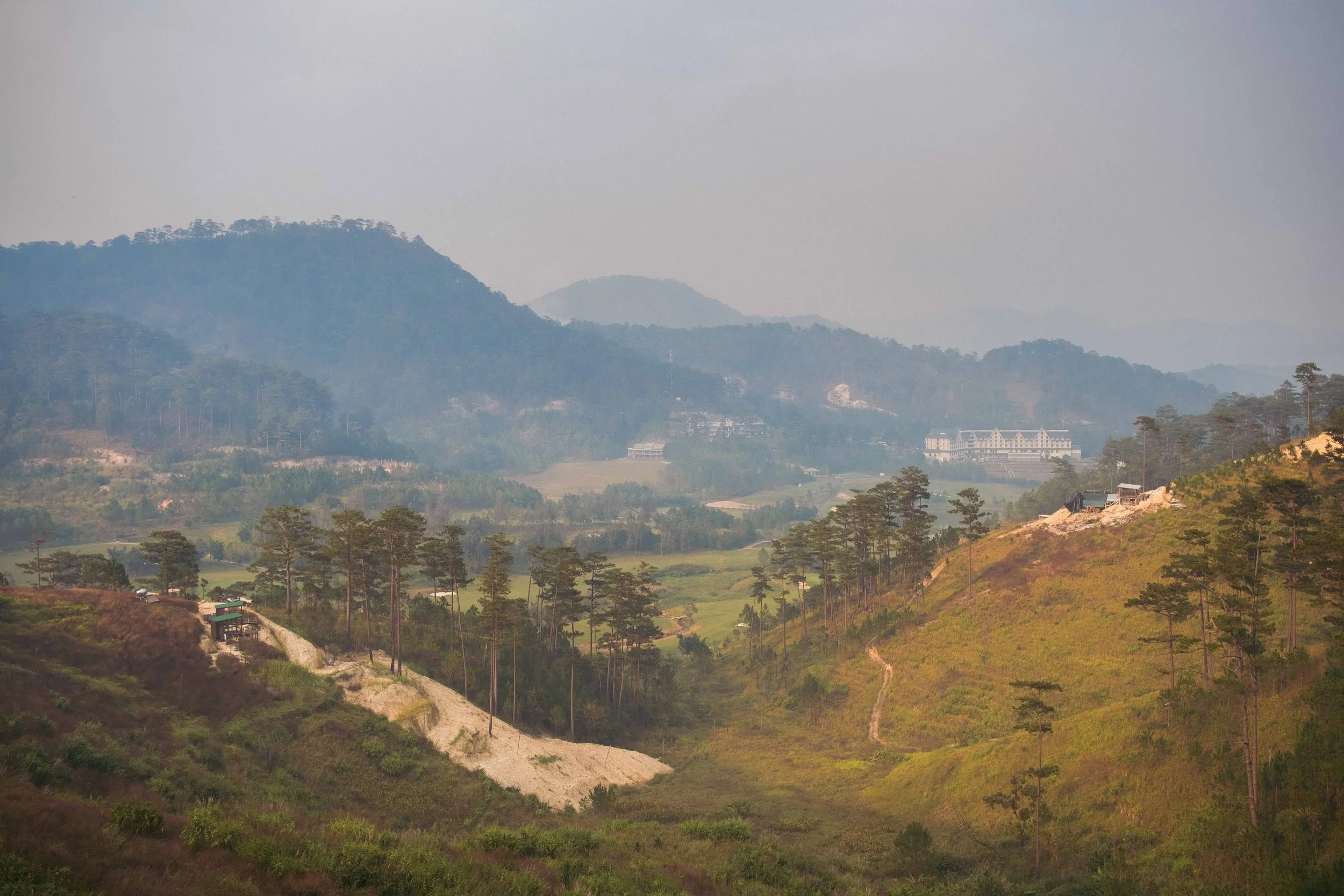 Mountains covered with trees and some buildings in the valley, with a cloudy sky.
