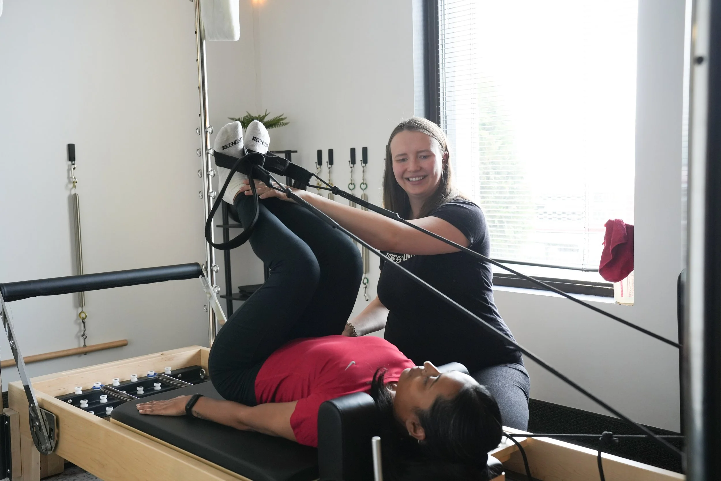 pregnant trainer smiling at client doing a Pilates reformer exercise