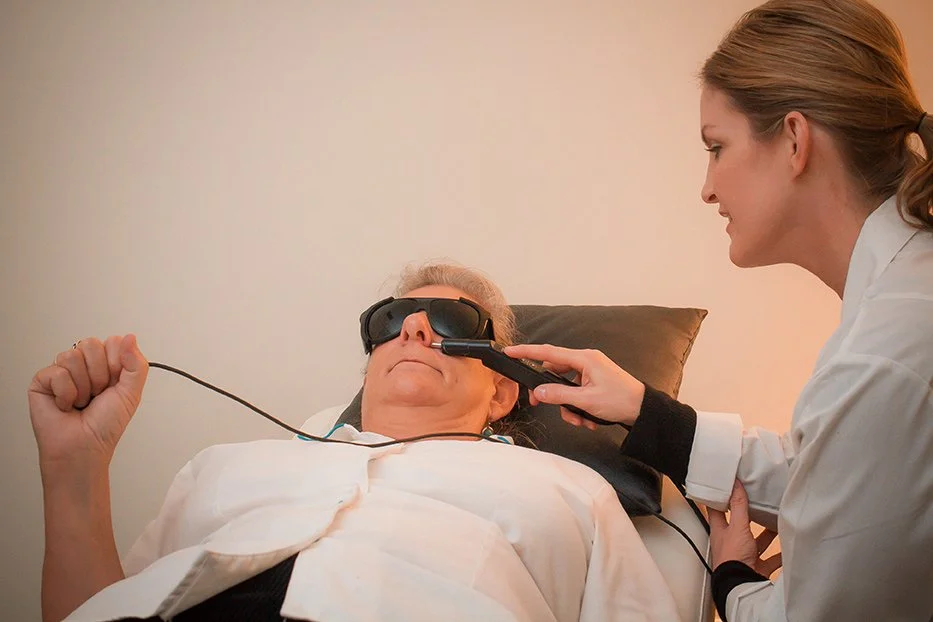 Laser Technician providing laser treatment to a client, who is laying on a treatment bed with protective goggles on