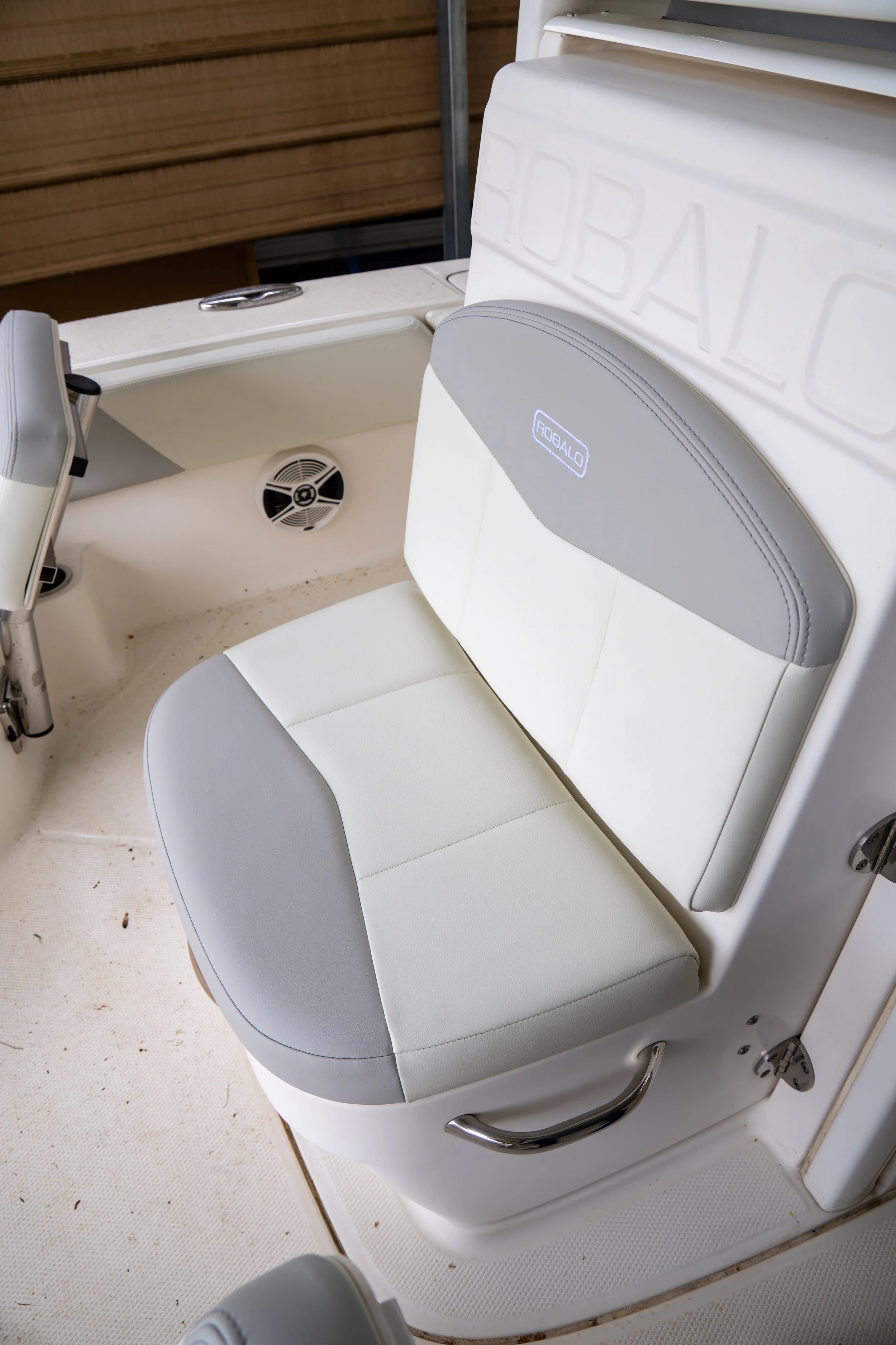 Close-up view of a white boat seat with gray accents and the brand name 'ROBAL' embossed on the backrest, with a wooden dock and boat hardware visible in the background.