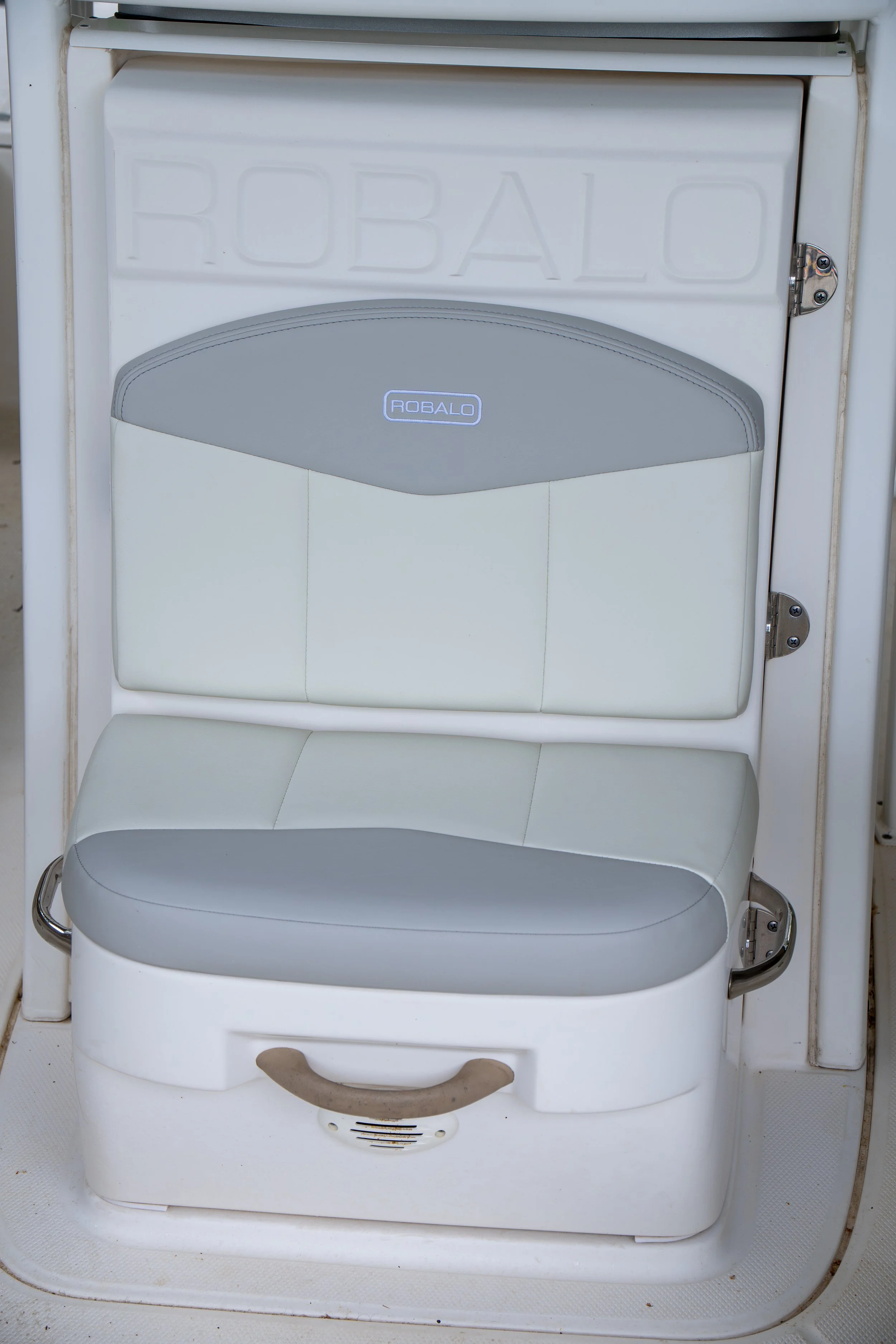 Front of a white robotic lawn mower with a gray top and beige handle, labeled 'ROBAL' on the front, on a white textured surface.