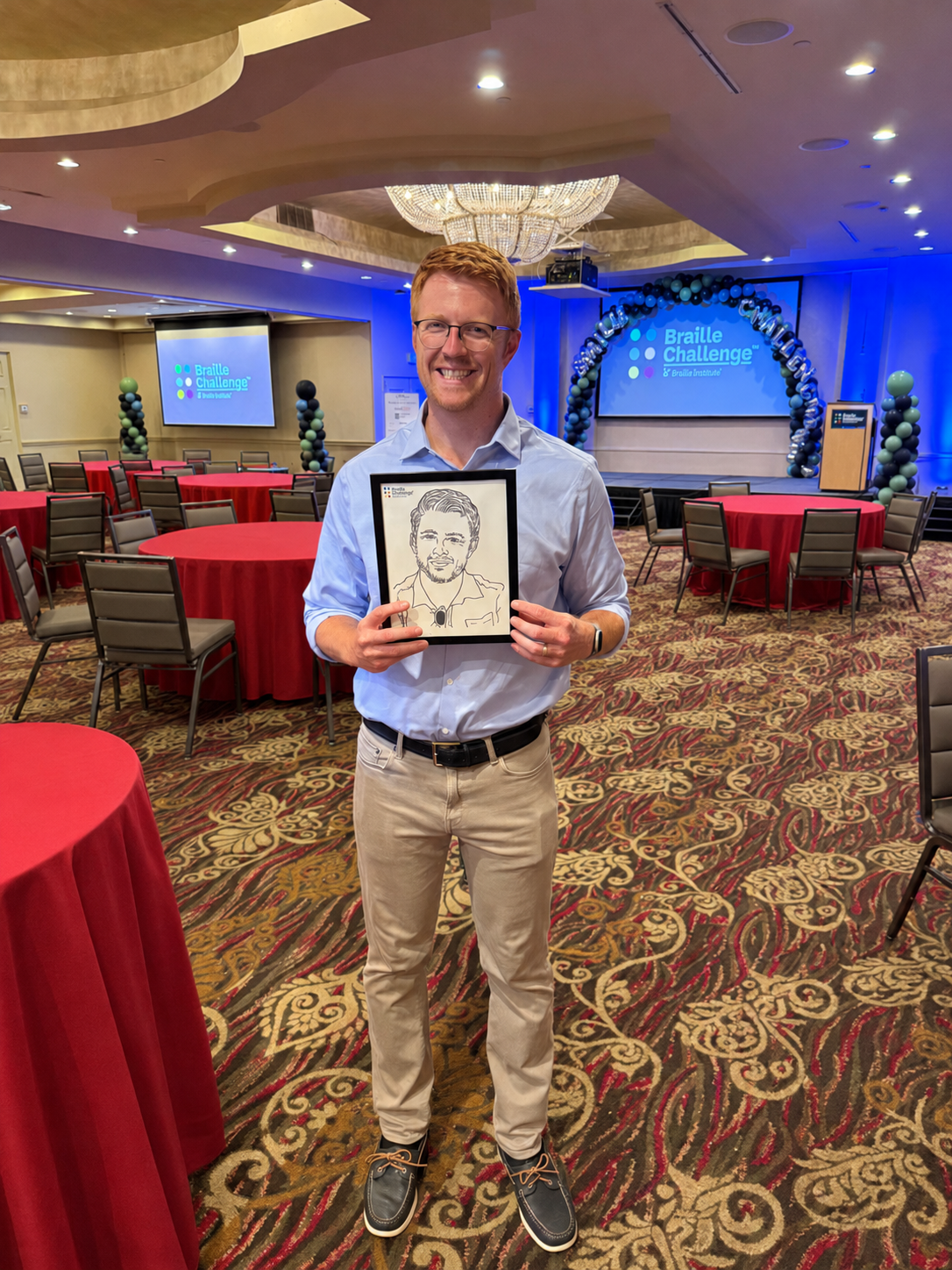 Mike Mulligan smiles while holding a tactile portrait of himself at the Braille Challenge event.