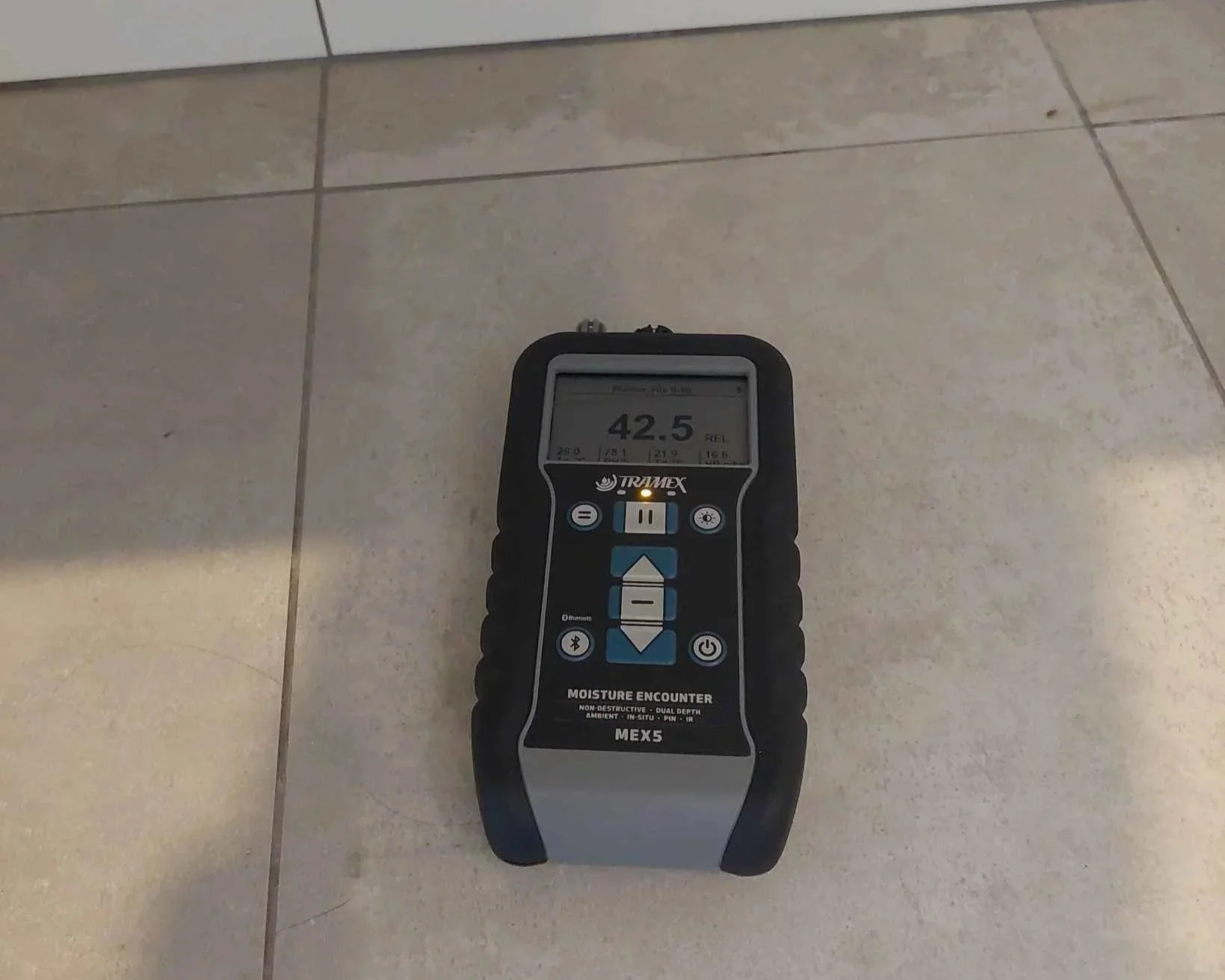 Baseline moisture reading taken on dry bathroom tile floor to establish control conditions before testing wet areas.