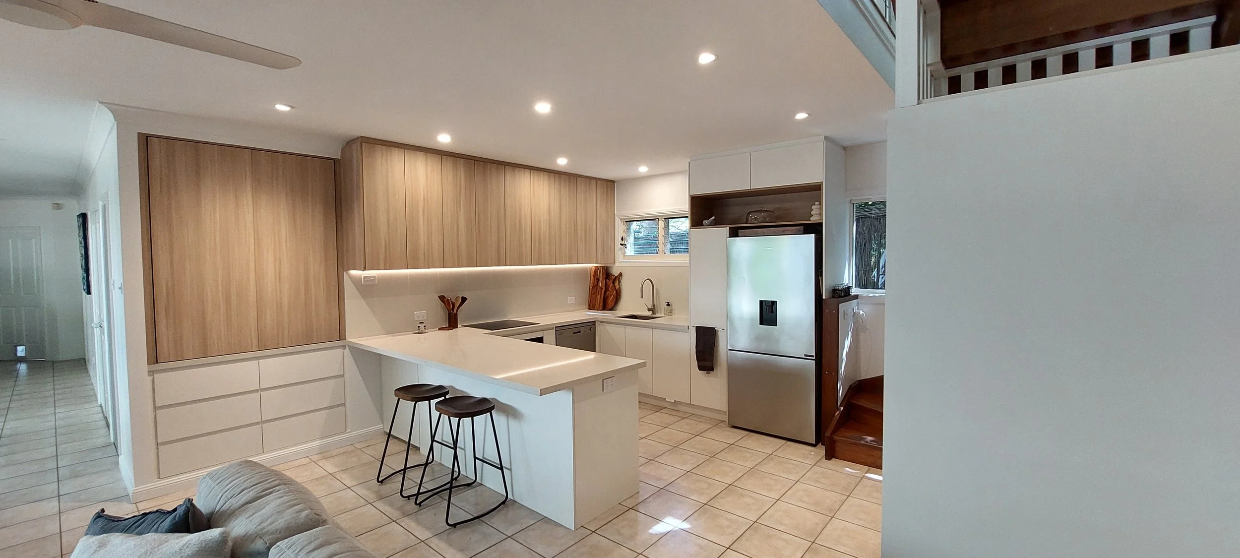 Modern kitchen with white cabinets, wooden accent wall, stainless steel refrigerator, and tiled floor. Includes a small island with two stools.