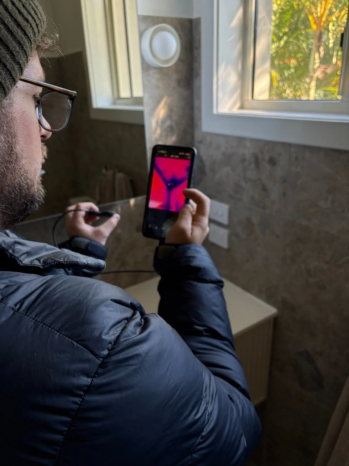 Builder using thermal imaging equipment to detect heat loss and moisture risk during a residential building performance inspection.