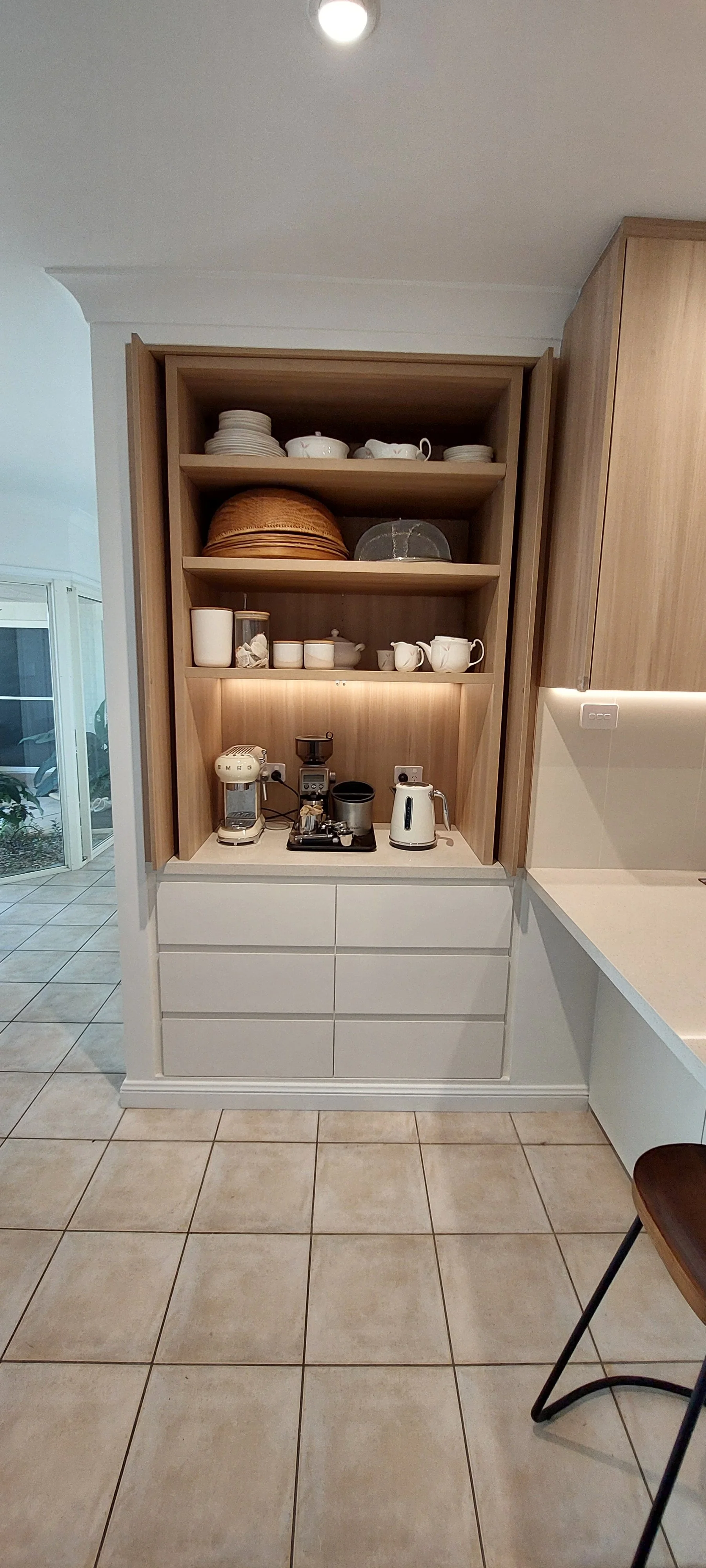 Kitchen shelf with dishes, cups, and appliances including a coffee maker, grinder, and kettle.