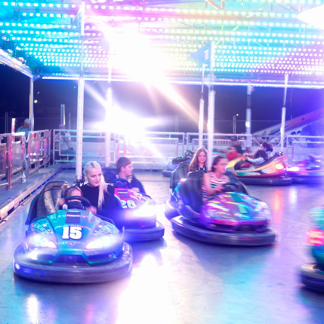 People riding bumper carts at a fair with really bright lights.