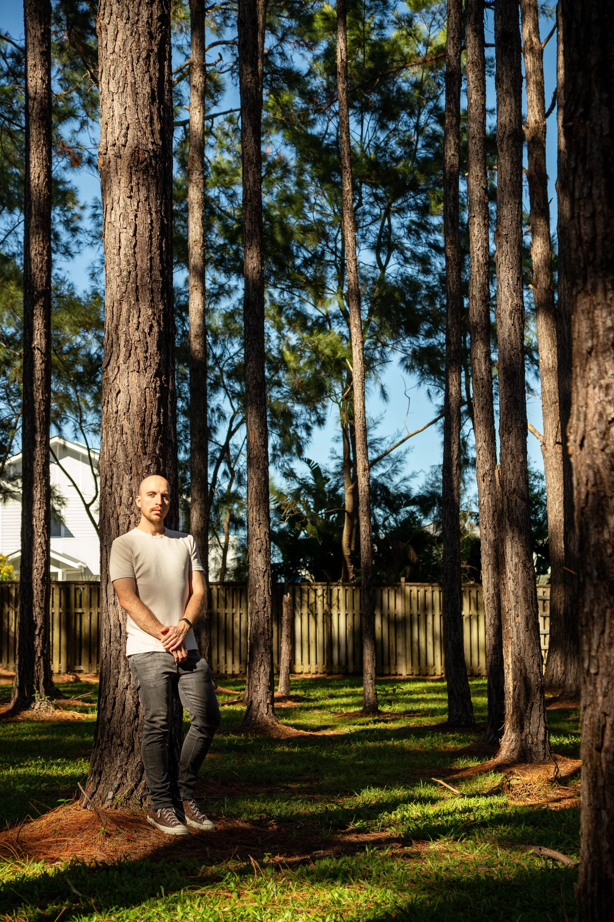Portrait of man leaning against pine tree in backyard forest, Coomera Waters.