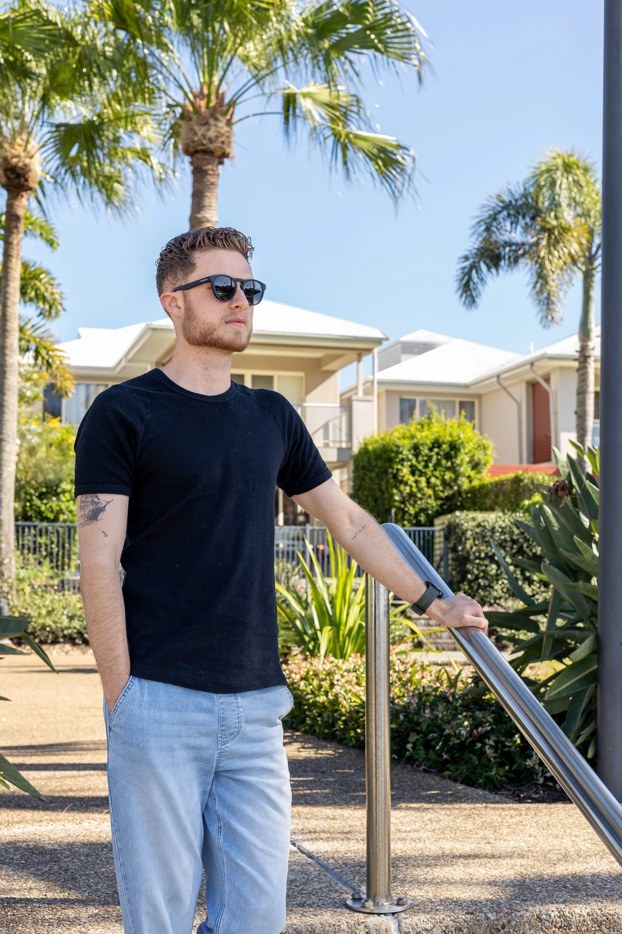 Personal branding portrait of man standing under palm trees in Coomera Waters with modern homes in background.