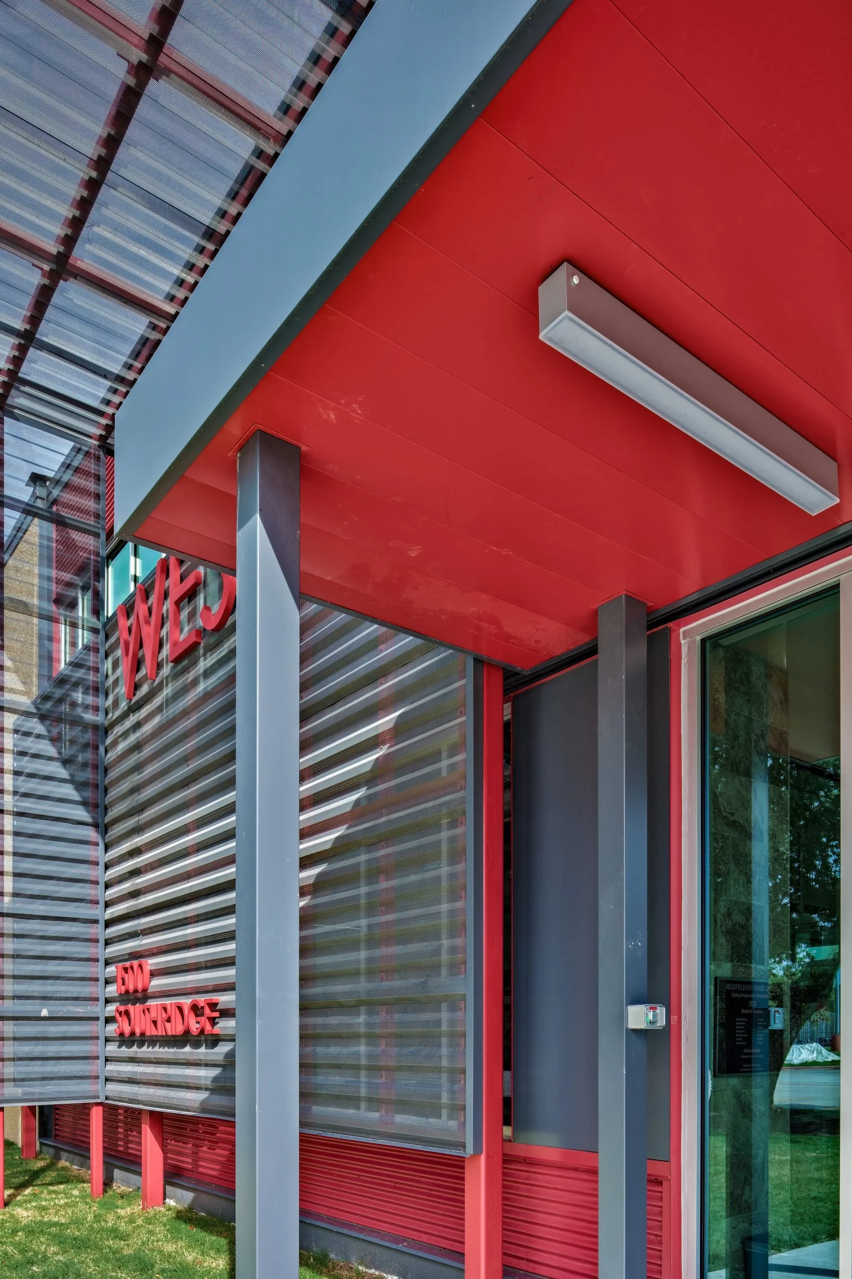 Close-up of modern building exterior with red and gray metal panels, large glass window, and red signage reading "WEX" and "SOURDGE."