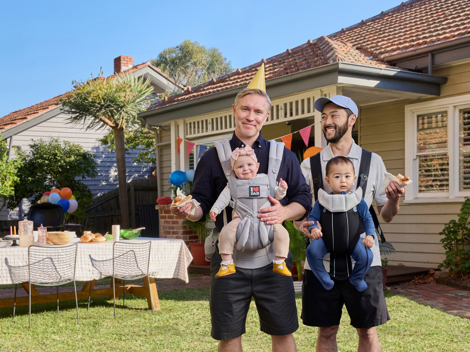 Two dads holding babies at BBQ