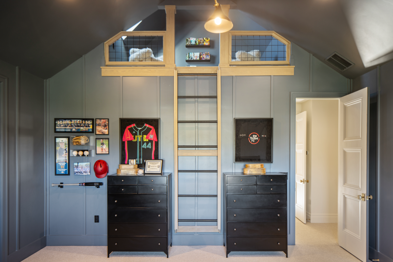 View of a bedroom with scout memorabilia, featuring two black dressers, sports jerseys, framed photos, and a white ladder leading to a loft with two beds.