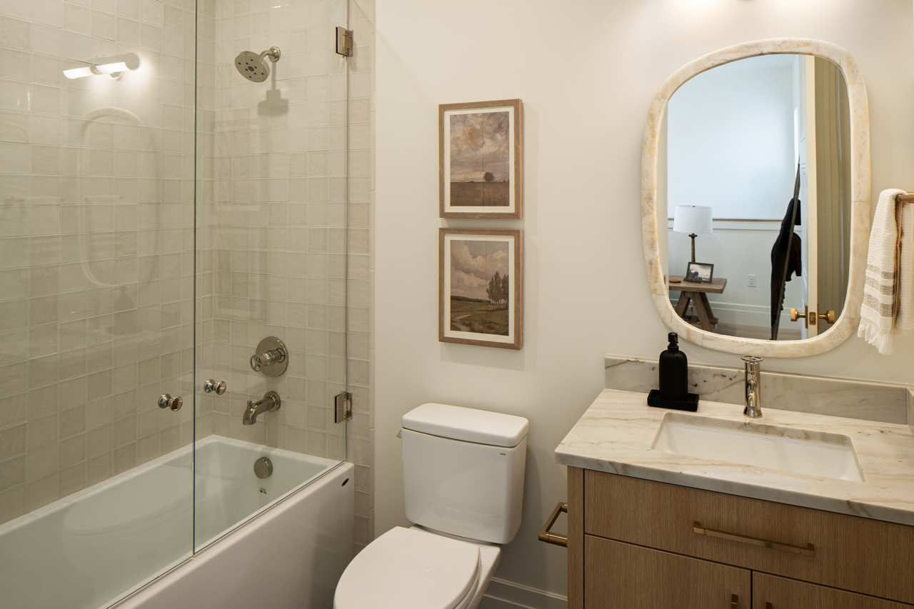 Contemporary bathroom with bathtub and shower, toilet, marble countertop sink, mirror, wall art, and a towel.