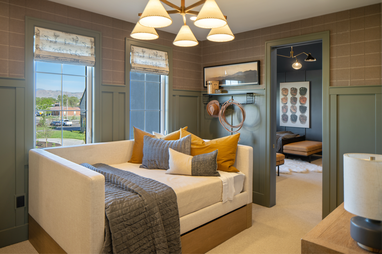 Cozy living room with beige couch, colorful pillows, and large windows with mountain view, adjacent to a bedroom with artwork and seating area.