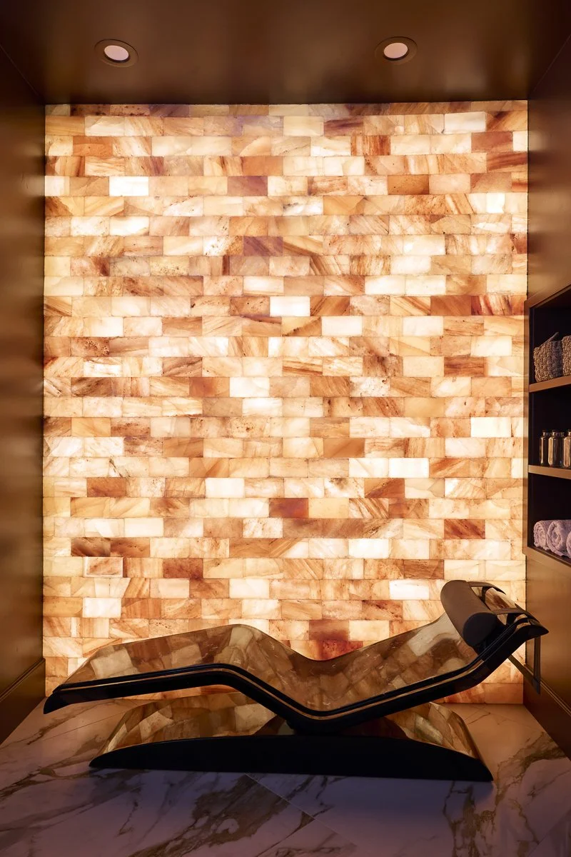 A relaxation lounge with a salt lamp wall and a curved lounge chair on a marble floor.