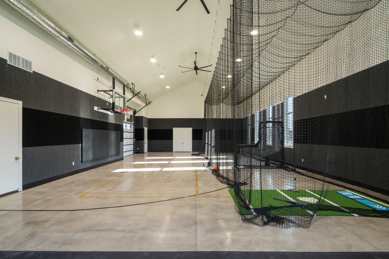 Indoor sports training facility with a basketball hoop, batting cage, and practice turf.