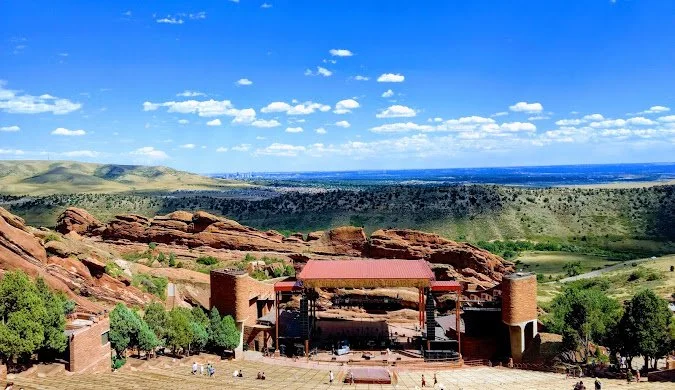 Outdoor amphitheater with red rock formations and a scenic landscape under a bright blue sky.