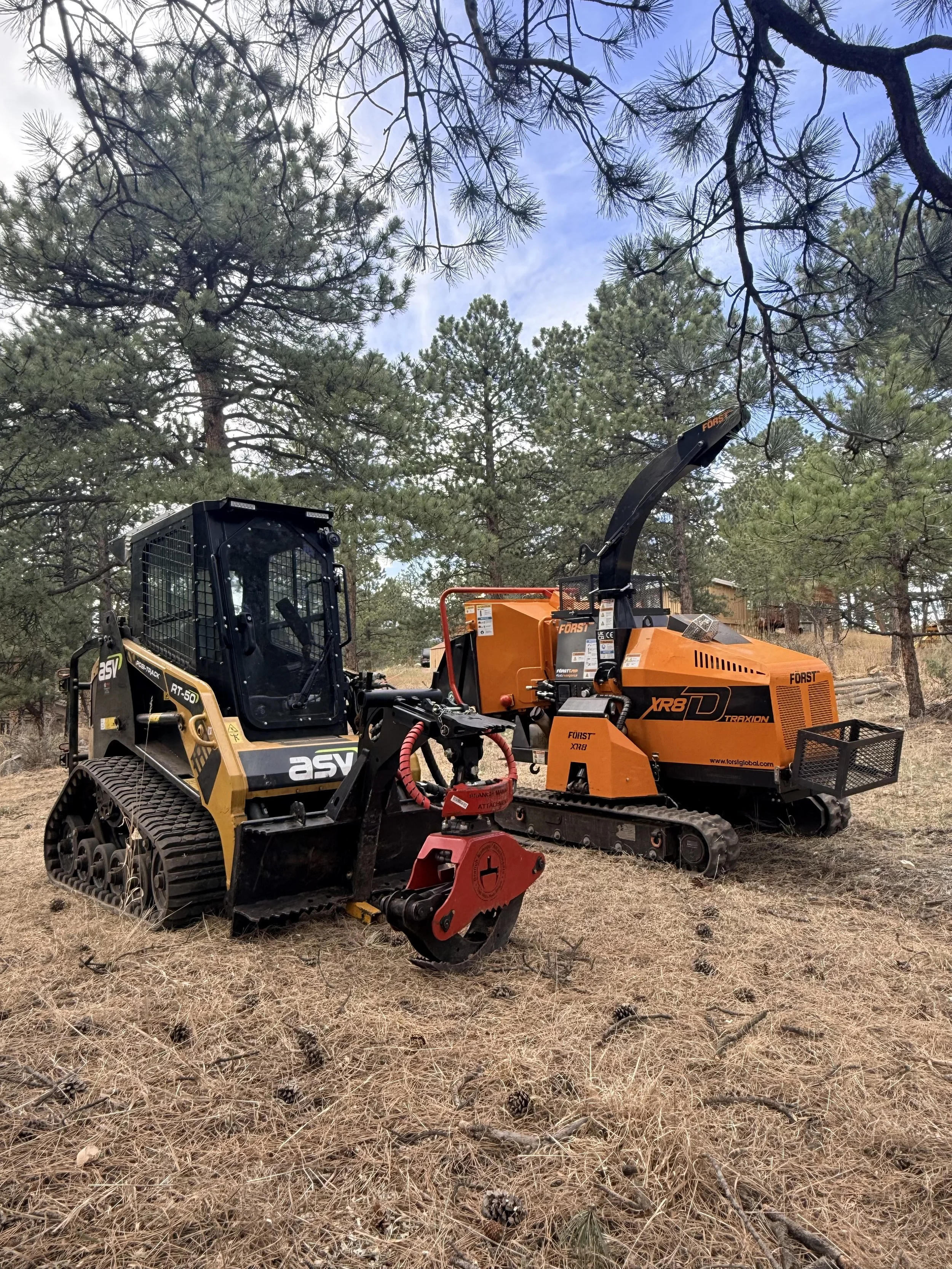 A skid steer and a FORST tracked chipper on a defensible space forestry work site in Evergreen Colorado