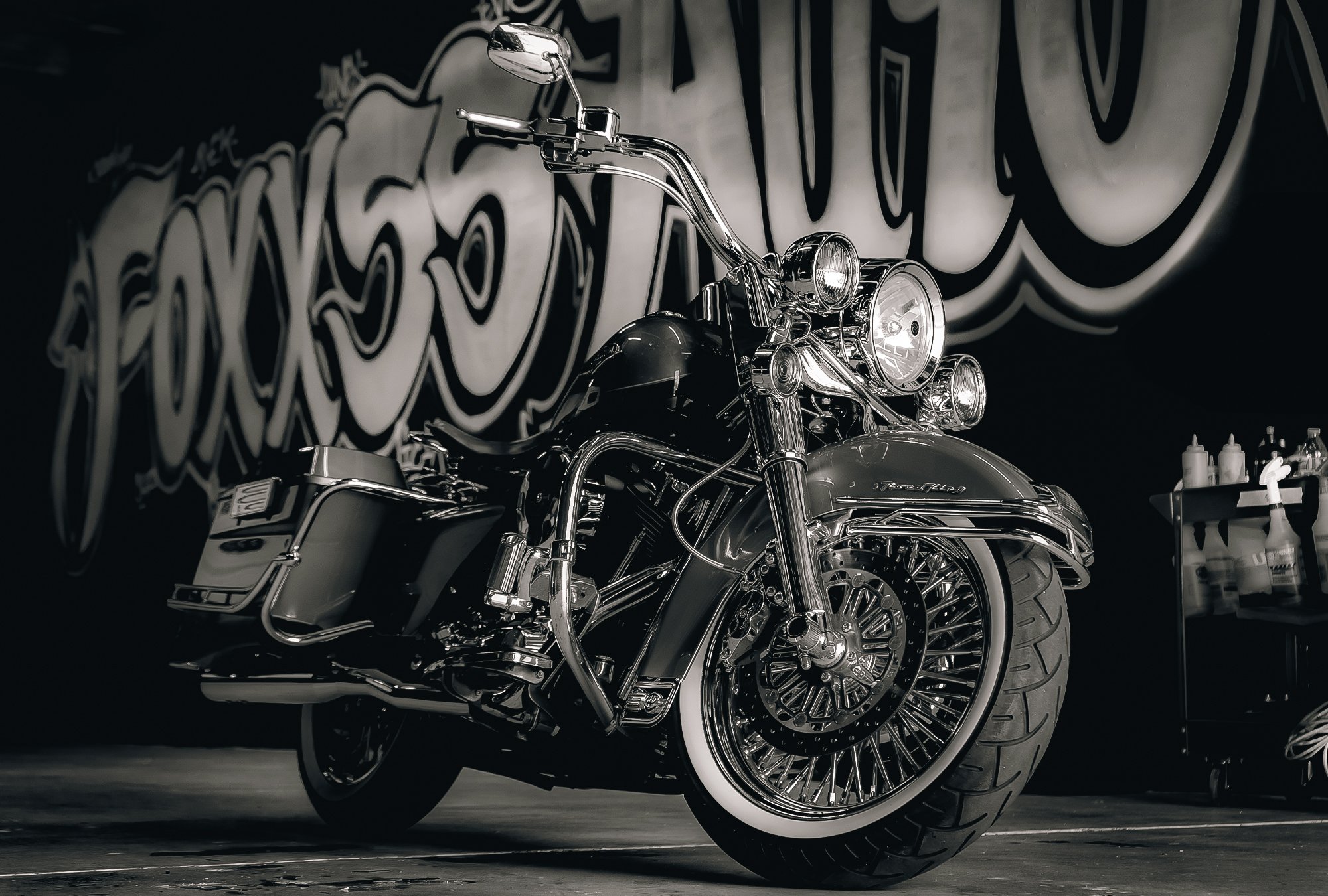 A black and chrome cruiser motorcycle parked indoors with a graffiti-style mural in the background.