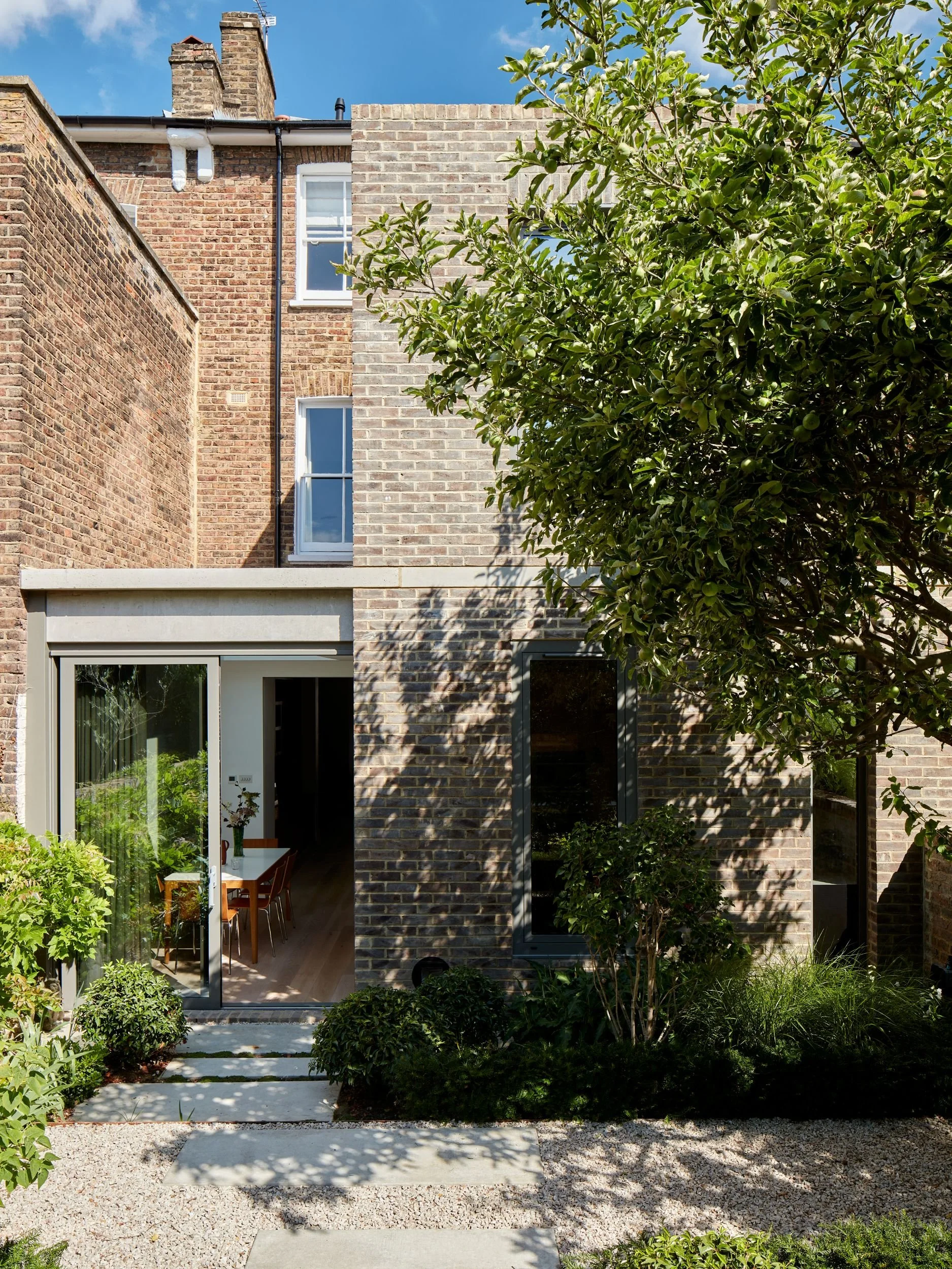 Modern brick house exterior with sliding glass doors, surrounded by lush greenery and a small stone pathway.