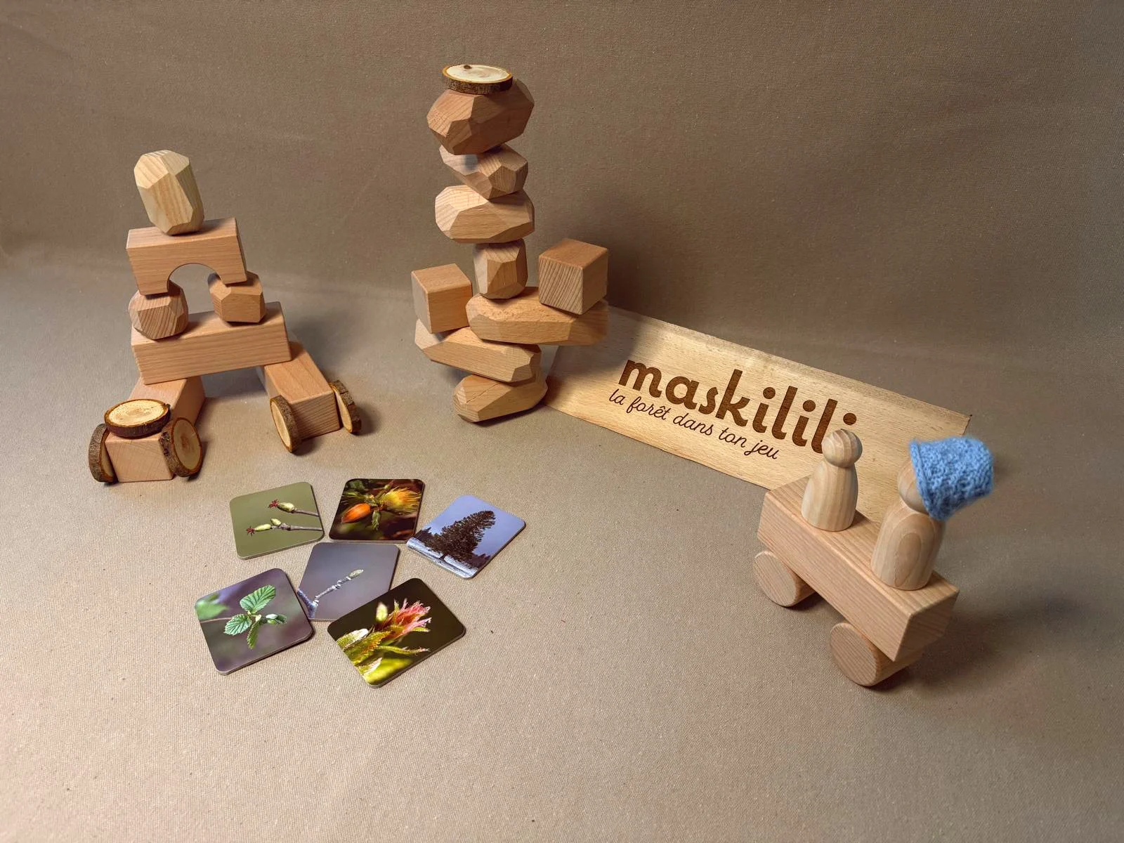 Jeu de société Maskil avec pièces en bois, figurines, cartes illustrées de plantes et nature, et un panneau avec le logo et la phrase "la forêt dans ton jeu".