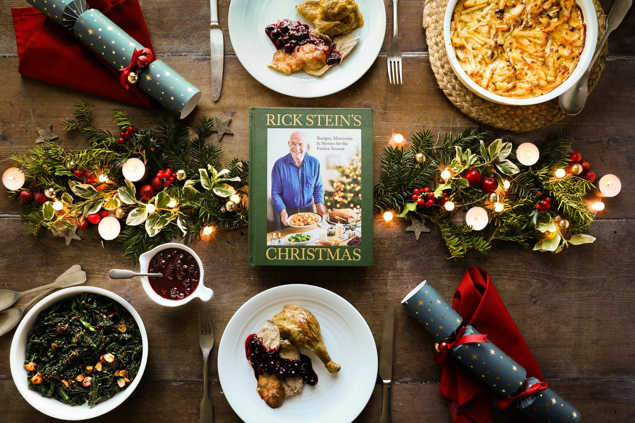 Editorial food photography and styling for The Happy Foodie for Penguin Random House publisher campaign. Cookbook titled 'Rick Stein Christmas' surrounded by plates of duck with cherry sauce, potatoes and vegetables 