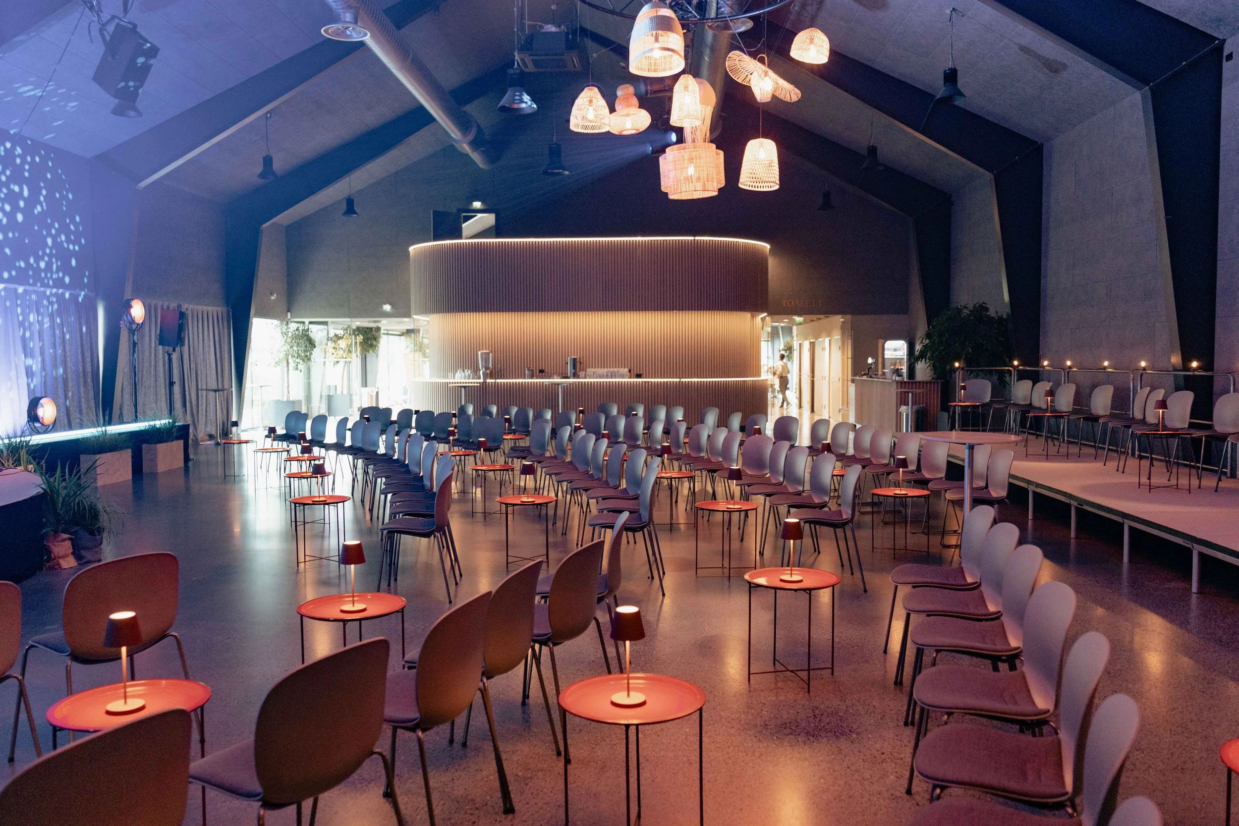 Moderne lounge med mange stoler, små bord, bar og dekorative pendellamper i et konferanselokale. 