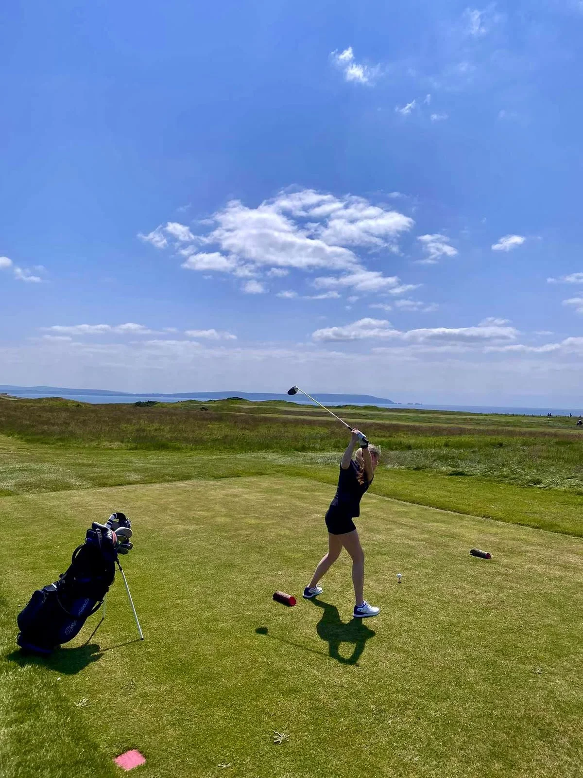 Barton-on-Sea golf course, on a beautiful sunny day, with bright blue skies and beautiful coastal scenery. Lois, a chiropractor at The Chewton Chiropractor is Teeing off, golf swing.