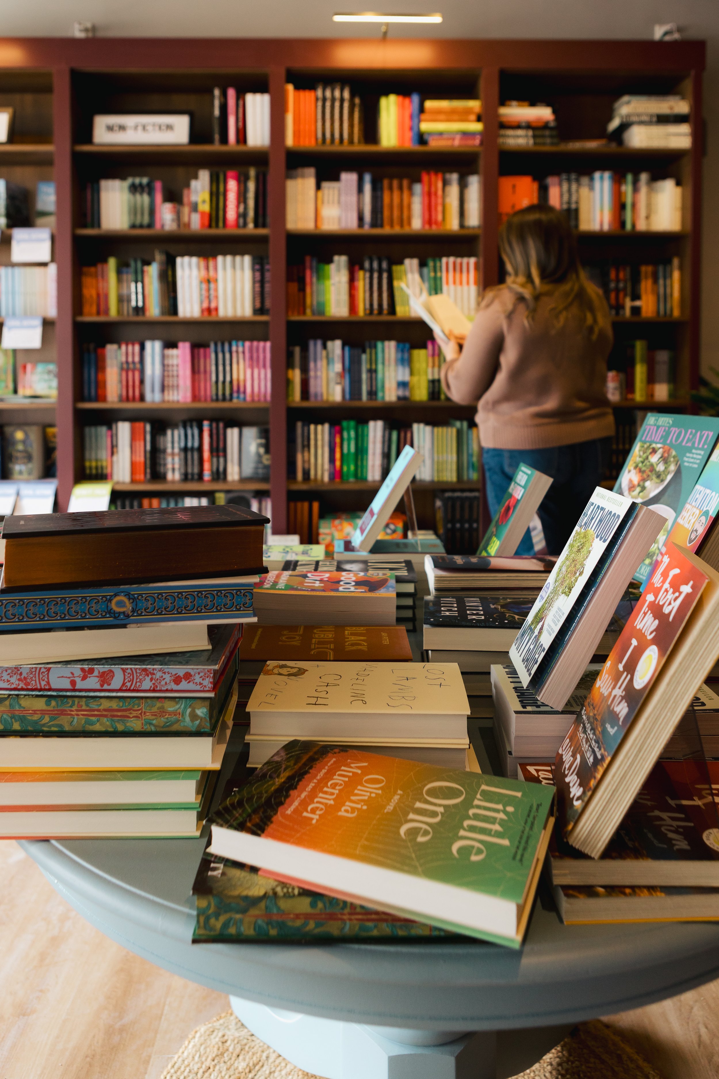 A woman with brown hair looking at a bookshelf filled with colorful books inside a bookstore or library.