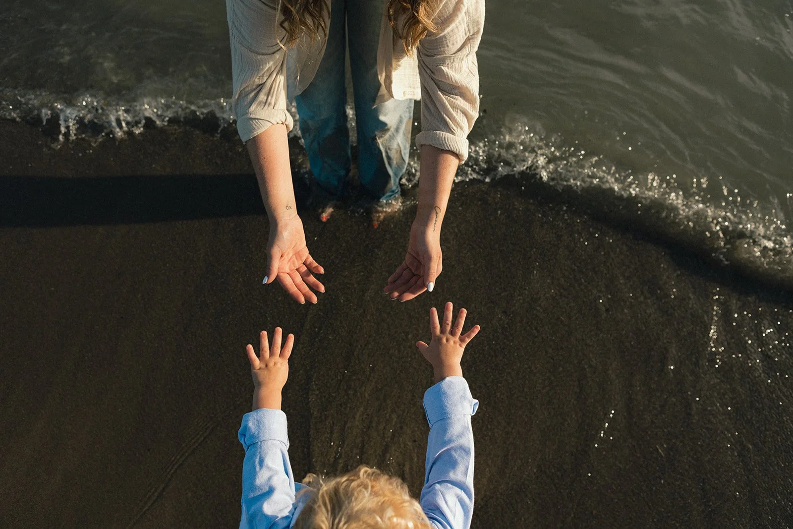 mother and son reaching for one another hands on beach