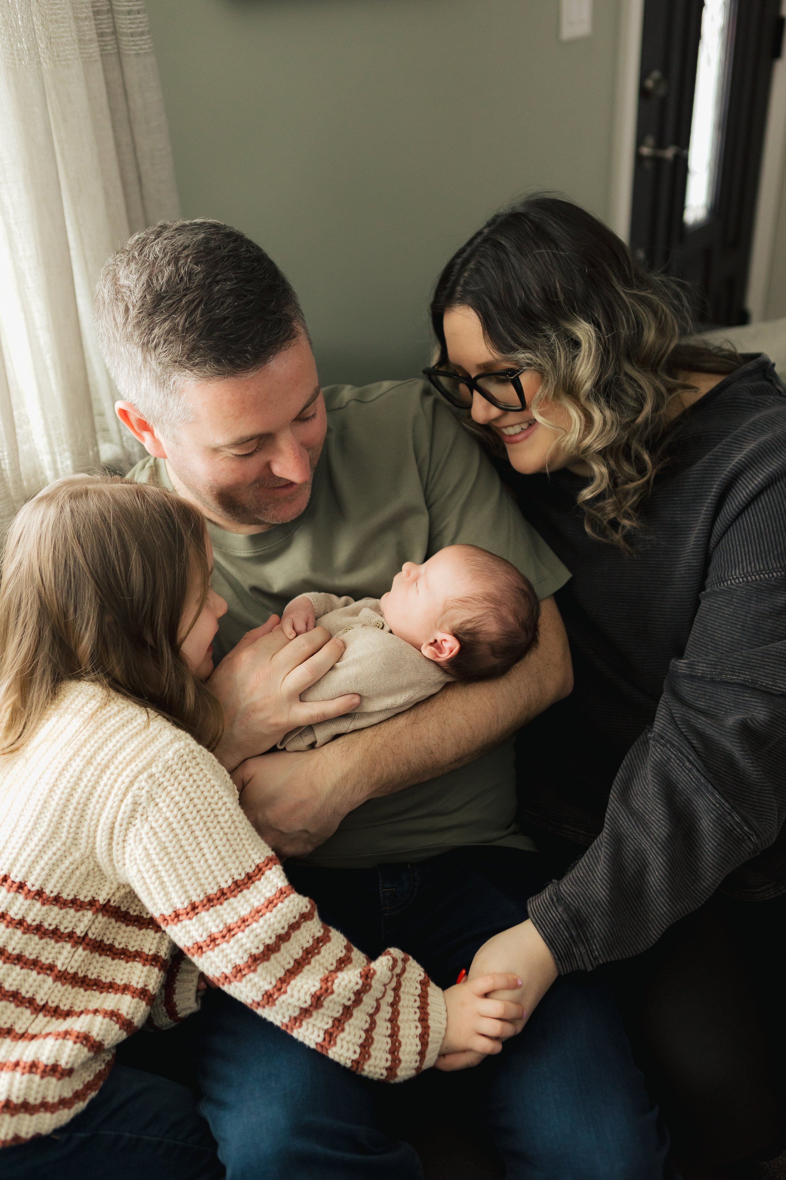 A family with a father, mother, young girl, and newborn baby in a cozy home setting.