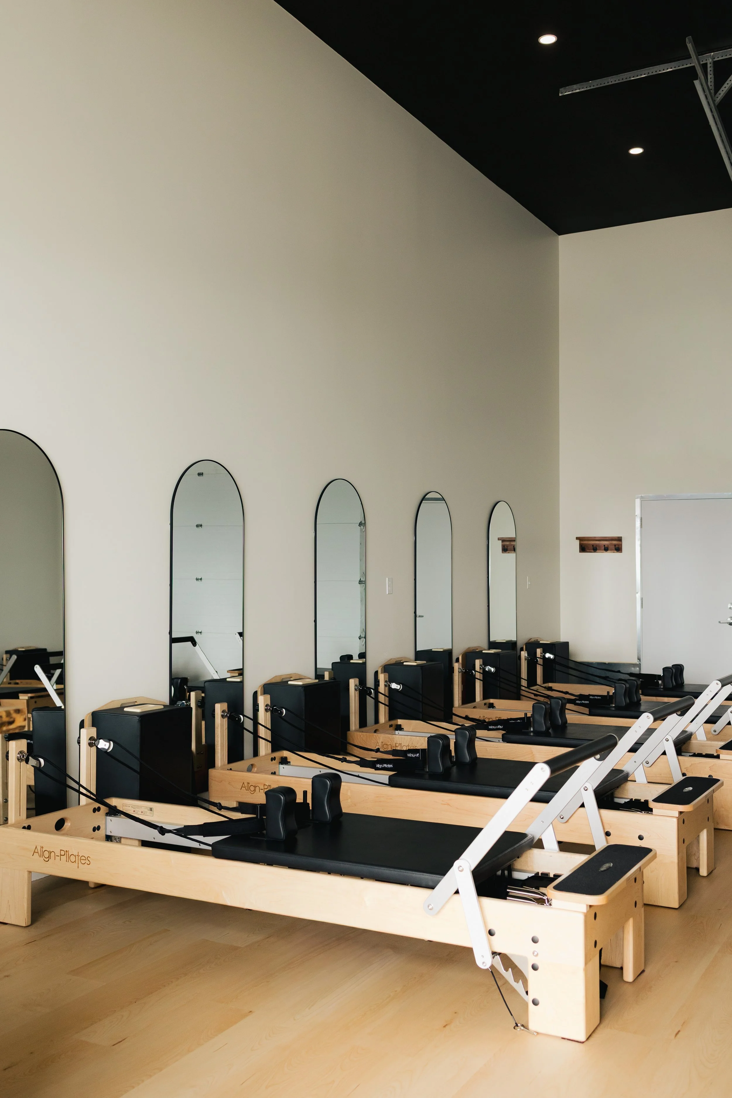 Row of reformer Pilates machines with mirrors on wall in a modern exercise studio.