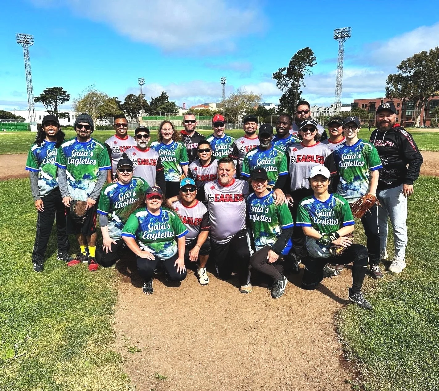Group of people in baseball gear on a baseball field, smiling for a photo