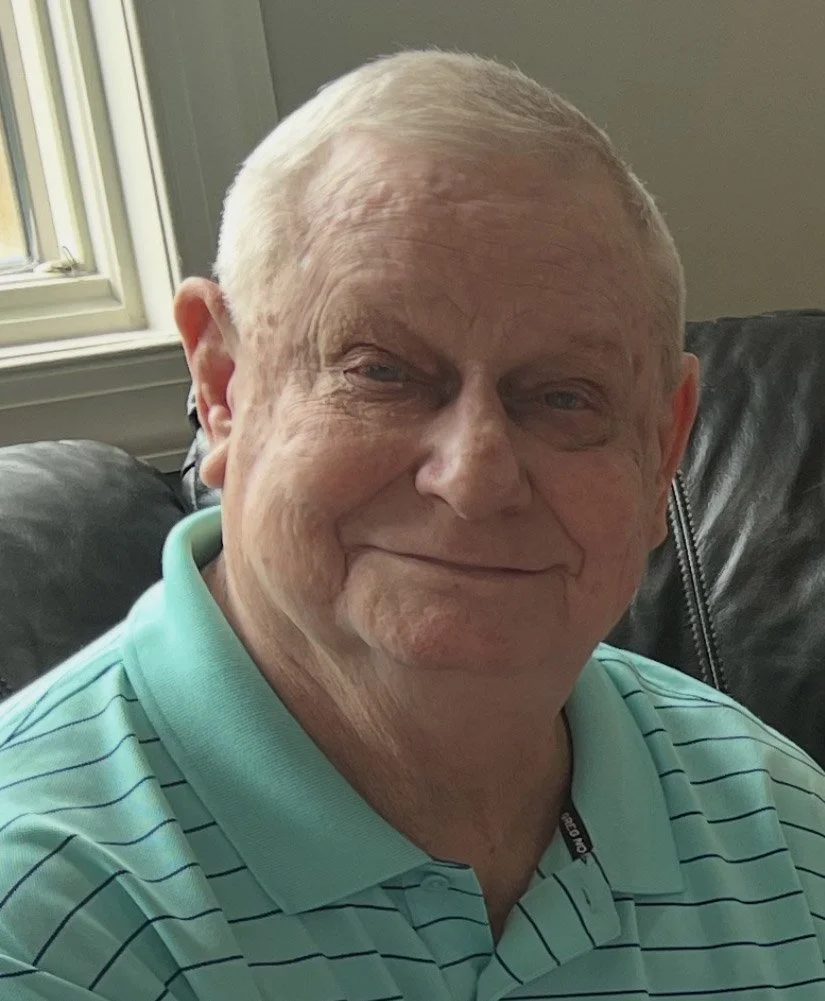 Close-up of a smiling older man with short gray hair, wearing a yellow shirt.