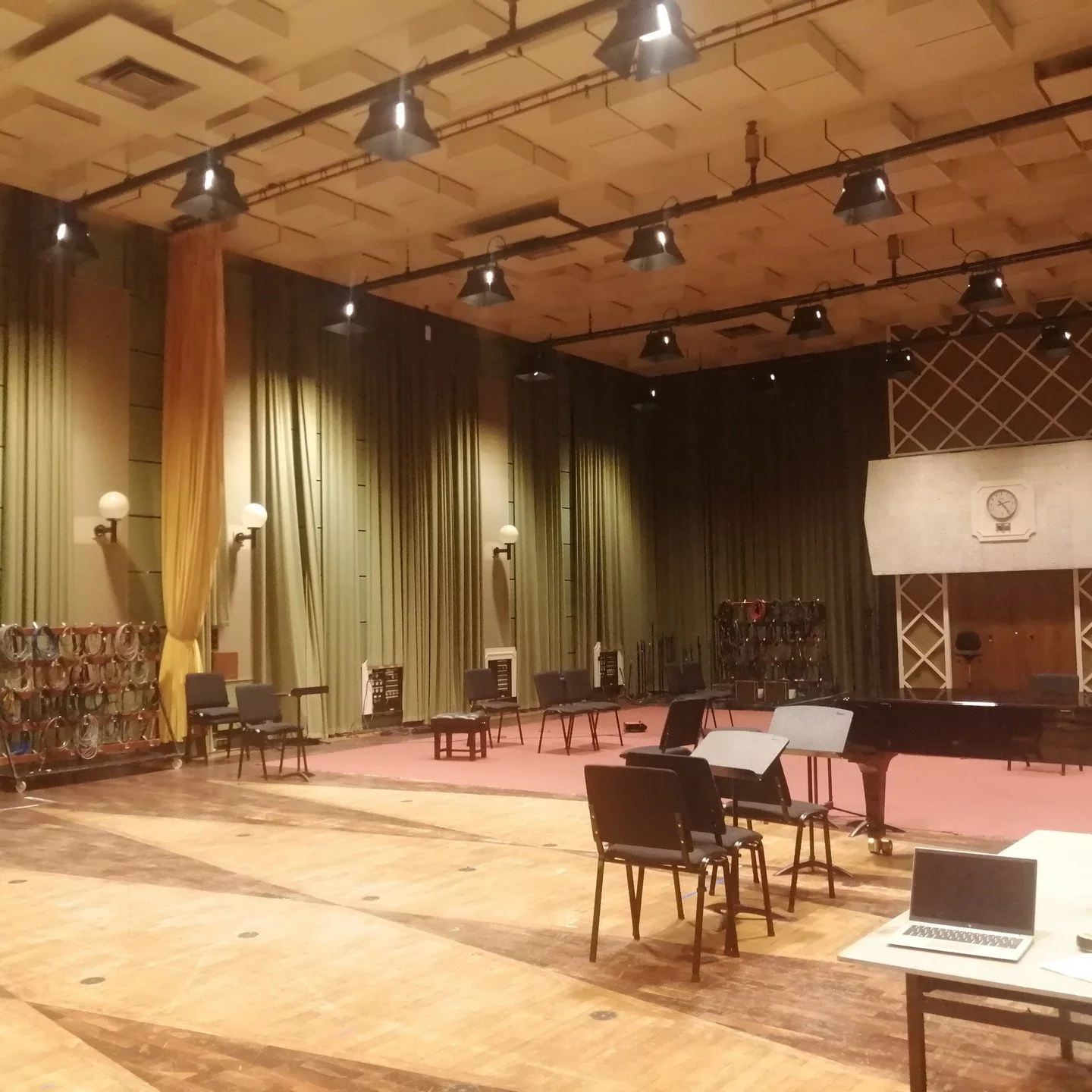 An empty theater or performance stage with chairs, musical instruments, and green curtains, prepared for a rehearsal or event.