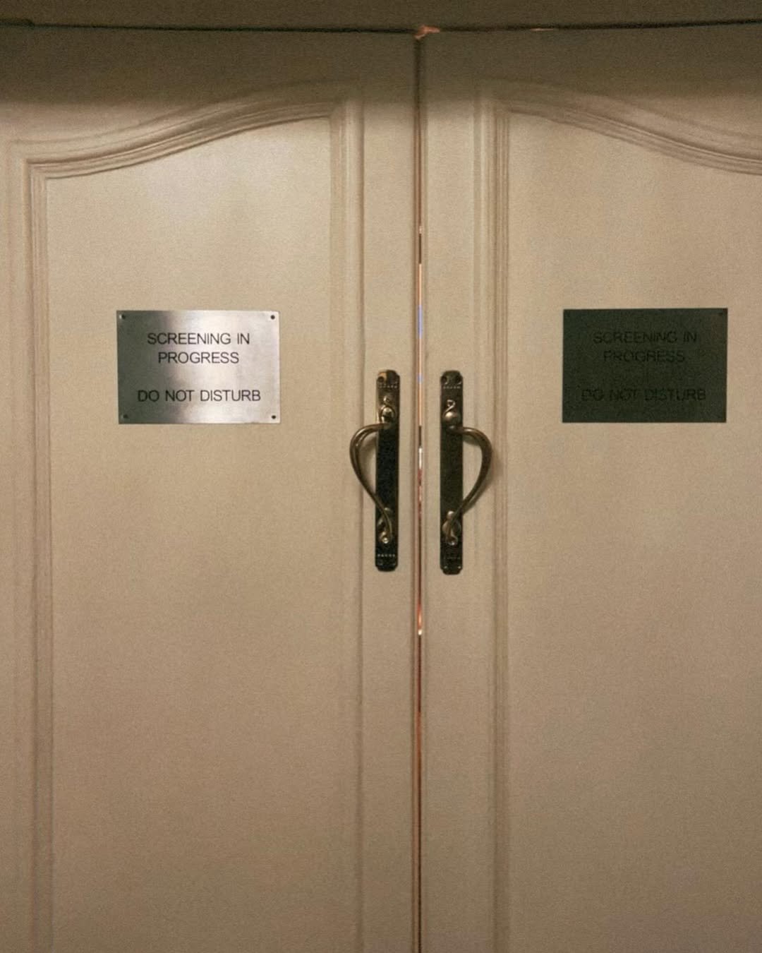 Double doors with signs that read "Screening in Progress Do Not Disturb".