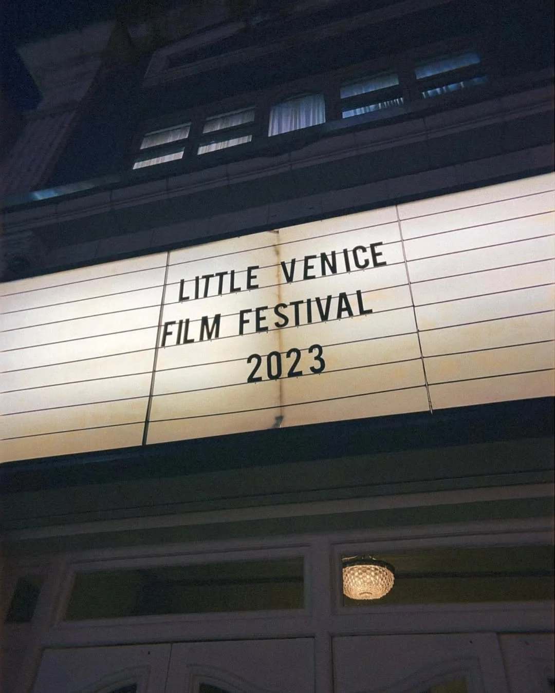 A marquee sign reads "Little Venice Film Festival 2023" outdoors at night, with a building and window reflection above the sign.
