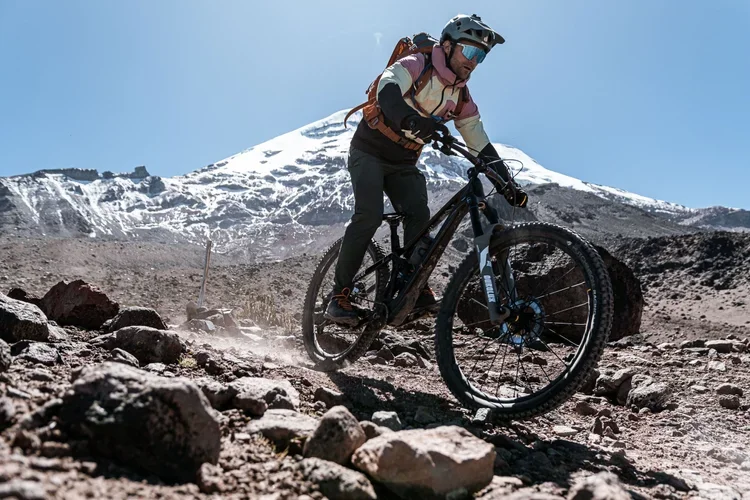 A man mountain biking on rocky terrain with snow-covered mountains in the background.
