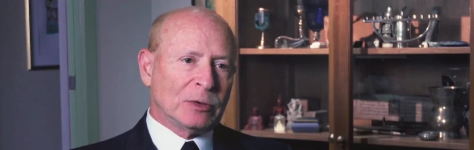 A middle-aged man in a suit being interviewed indoors
