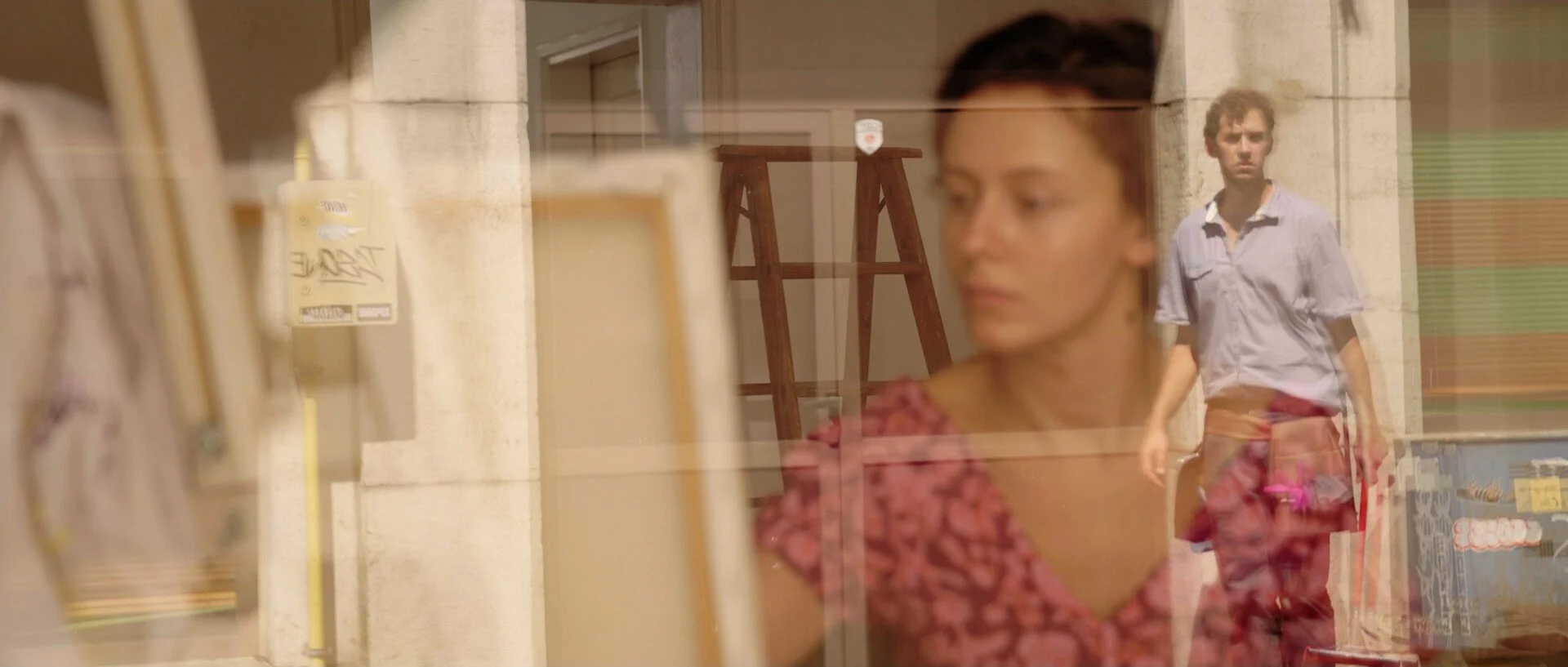 A woman looking at store shelves with a man walking behind her outside a store window.